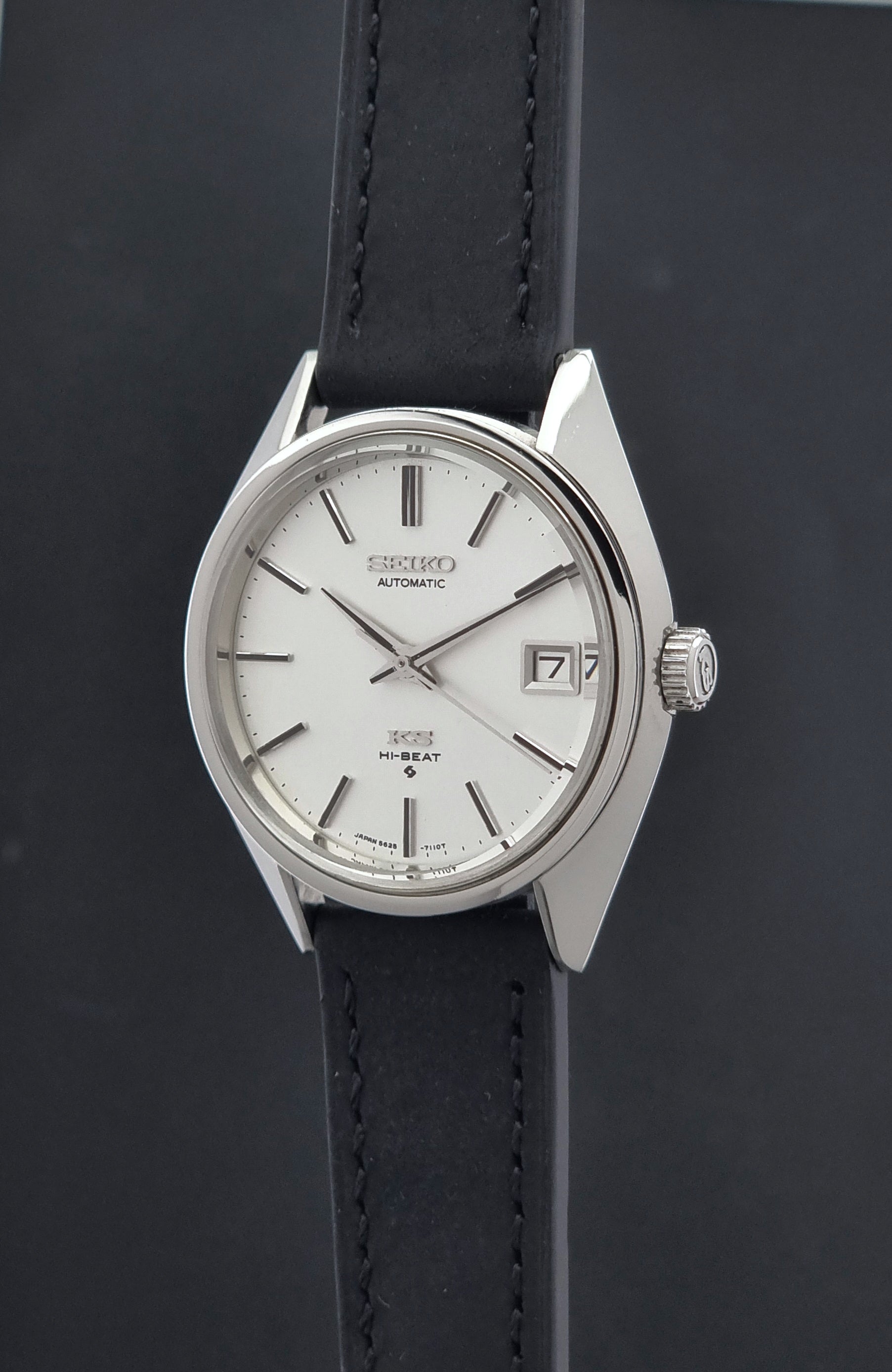 Vintage King Seiko 5625-7110 wristwatch with a silver-toned case, white dial, and black leather strap, shown against a dark gray background crown profile view