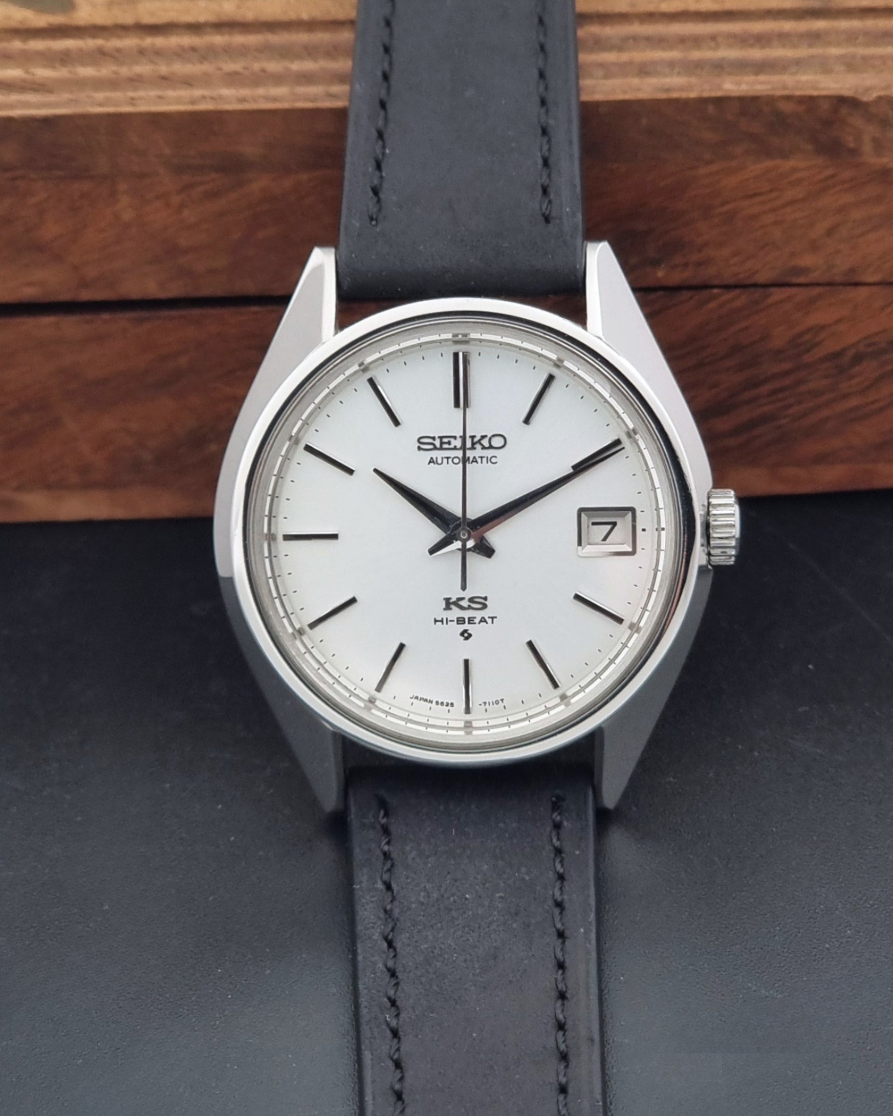 Vintage King Seiko 5625-7110 Wristwatch with a silver-toned metal case, white dial, and black leather strap, on a dark textured background dial view
