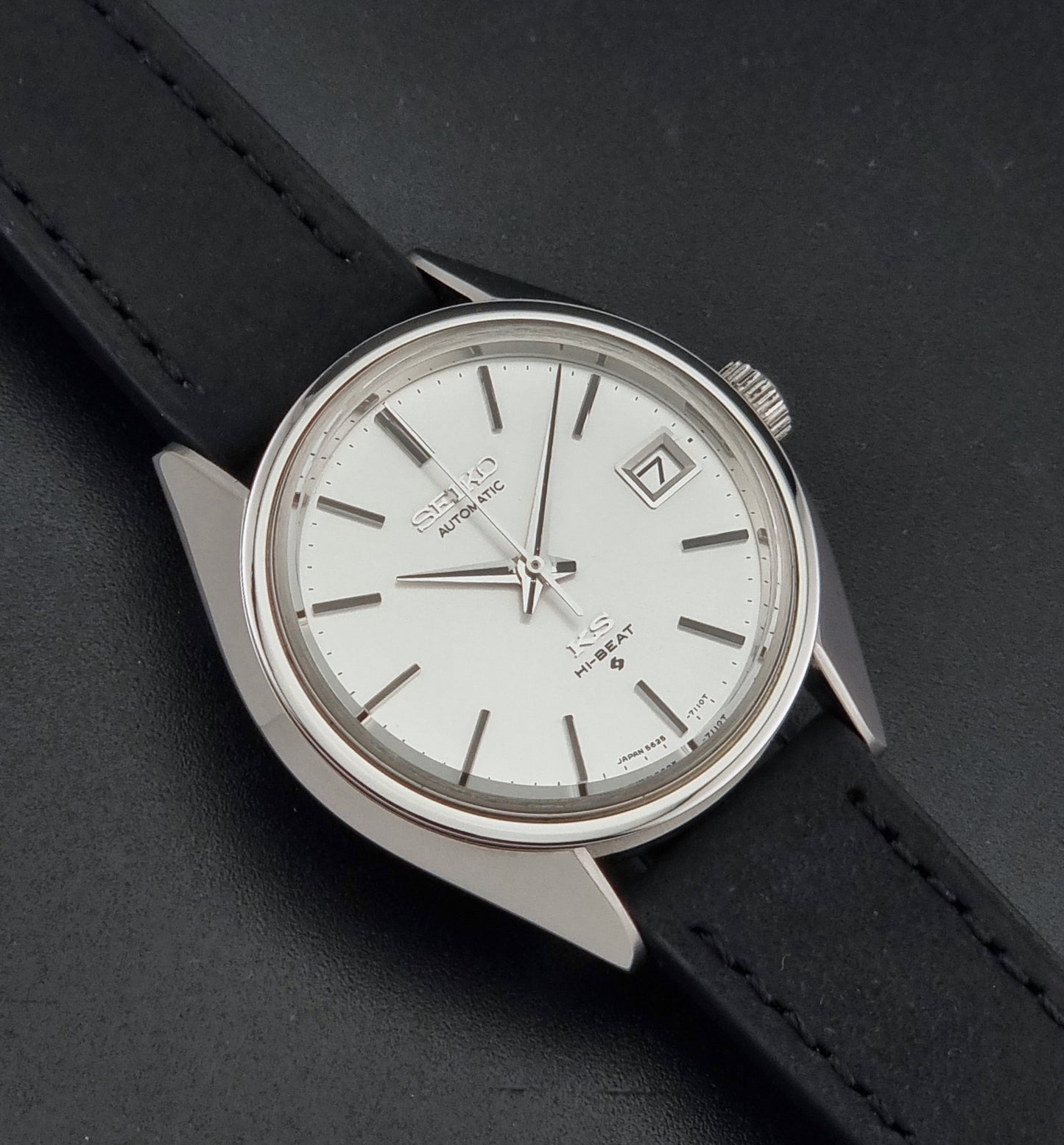 Vintage King Seiko 5625-7110 automatic wristwatch with a silver-toned metal case, white dial, and black strap, shown on a dark textured background close up dial view