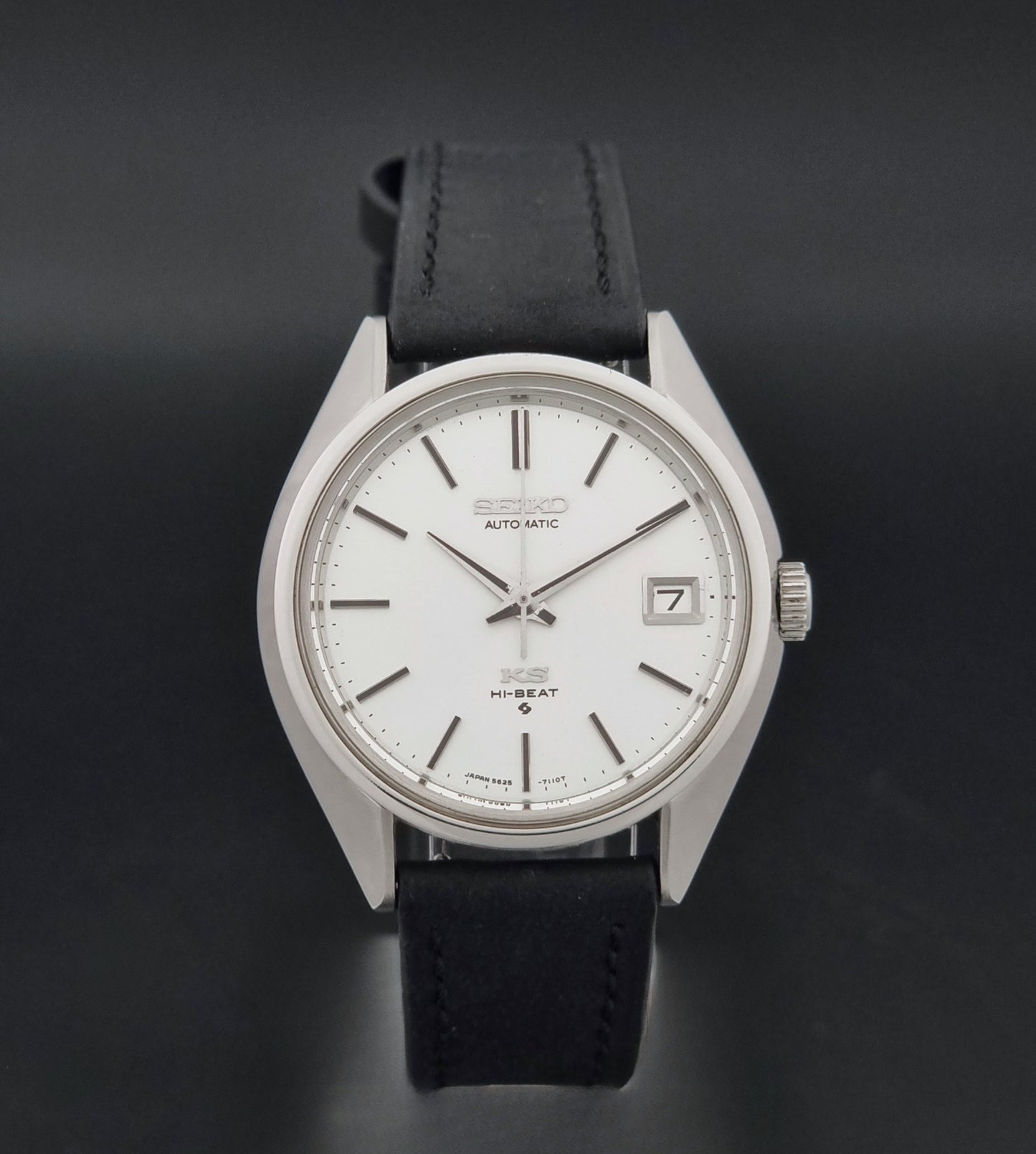 Vintage King Seiko 5625-7110 Wristwatch with a silver-toned metal case, white dial, and black leather strap, on a dark textured background close dial view