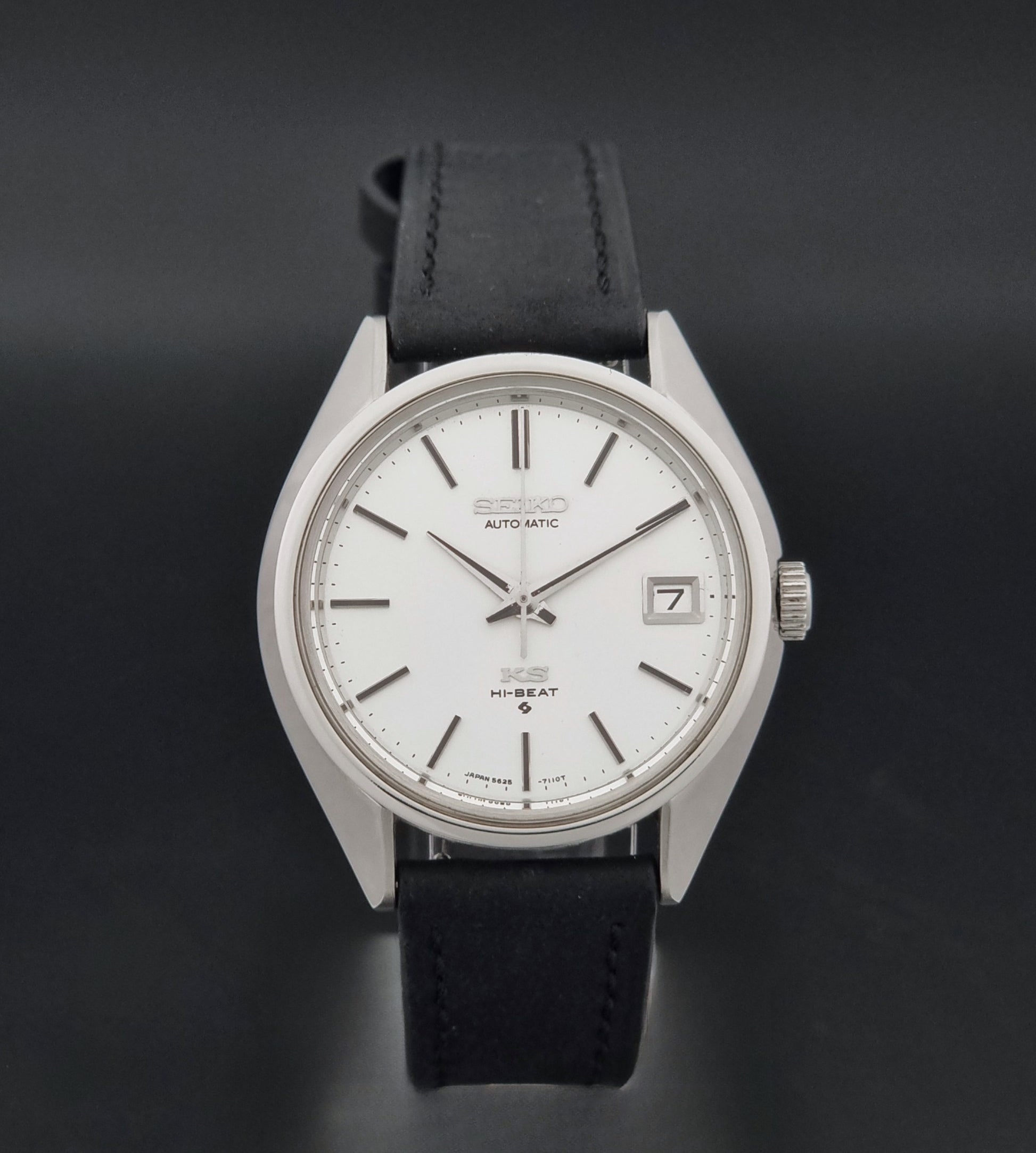 Vintage King Seiko 5625-7110 Wristwatch with a silver-toned metal case, white dial, and black leather strap, on a dark textured background close dial view