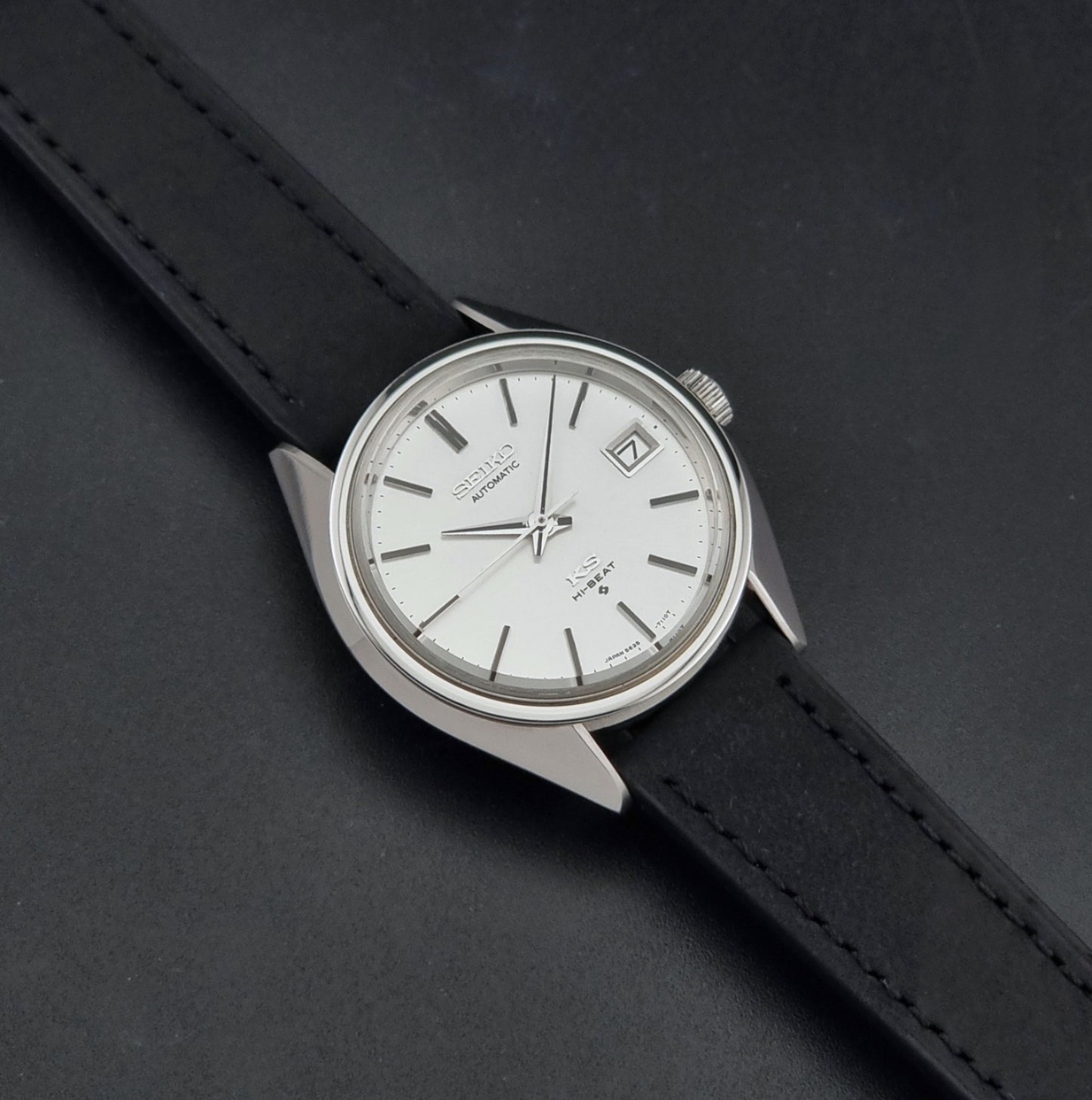 Vintage King Seiko 5625-7110 Wristwatch with a silver-toned metal case, white dial, and black leather strap, on a dark textured background dial