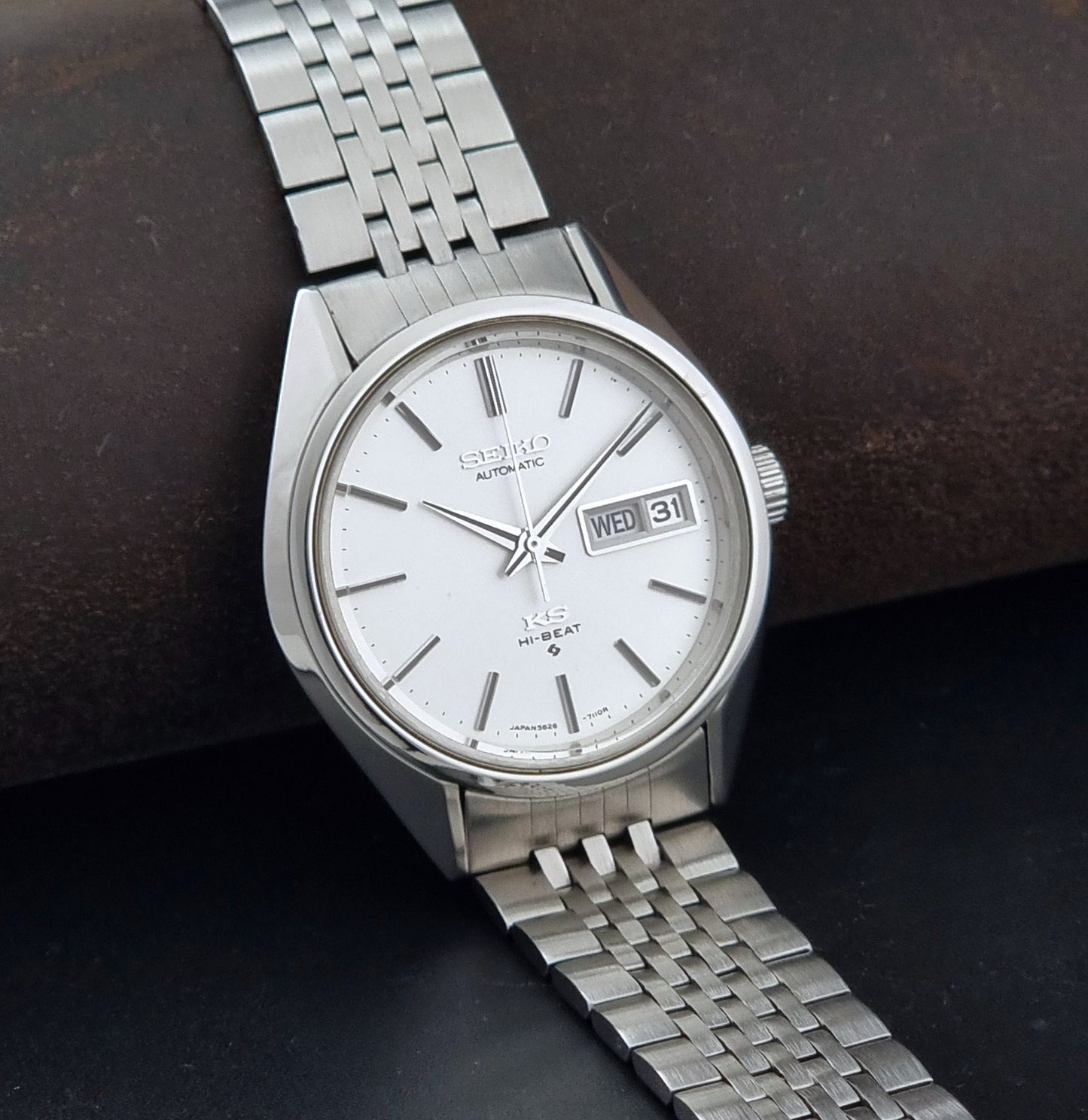 A vintage Seiko automatic watch with a silver stainless steel case and link bracelet, featuring a white dial with a day and date window.