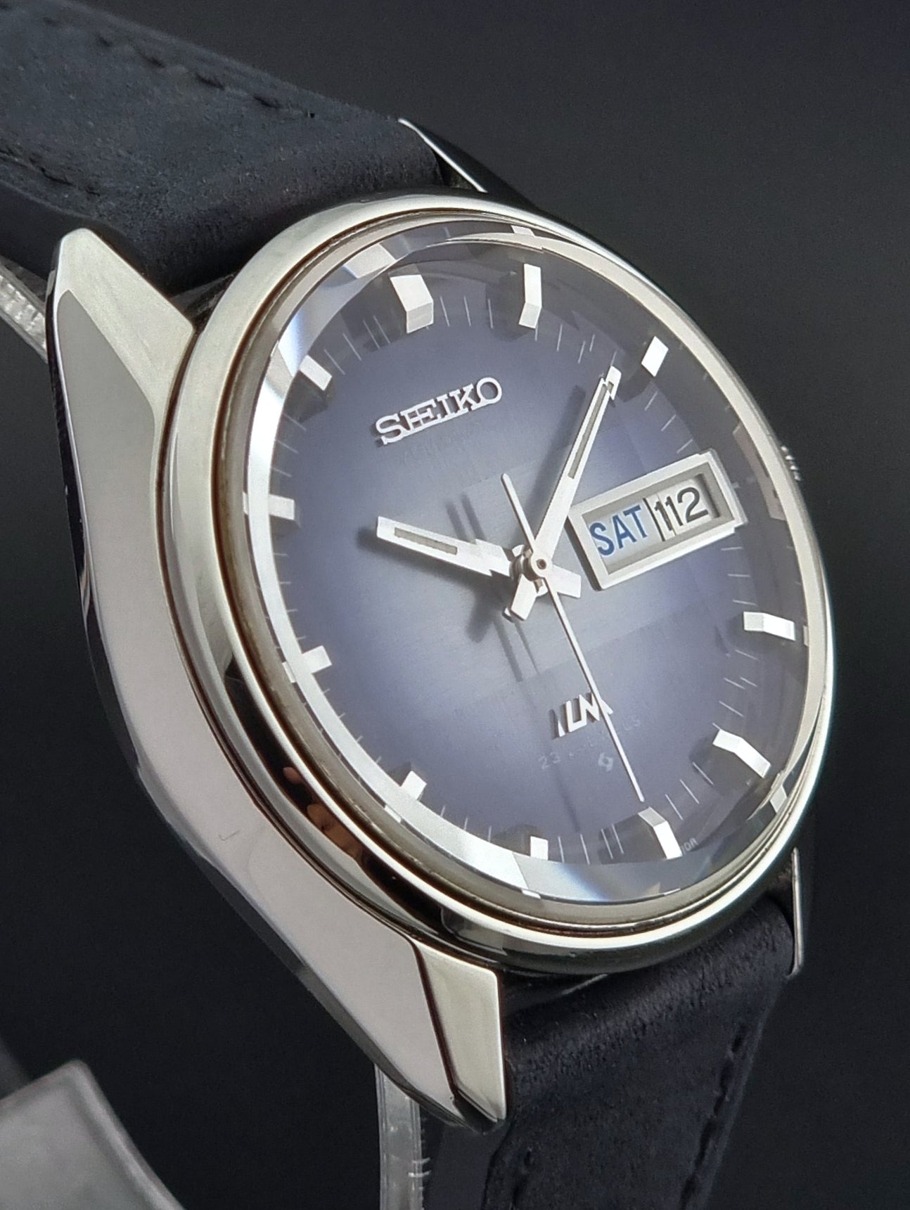 Seiko watch with blue face and black leather strap on a dark background