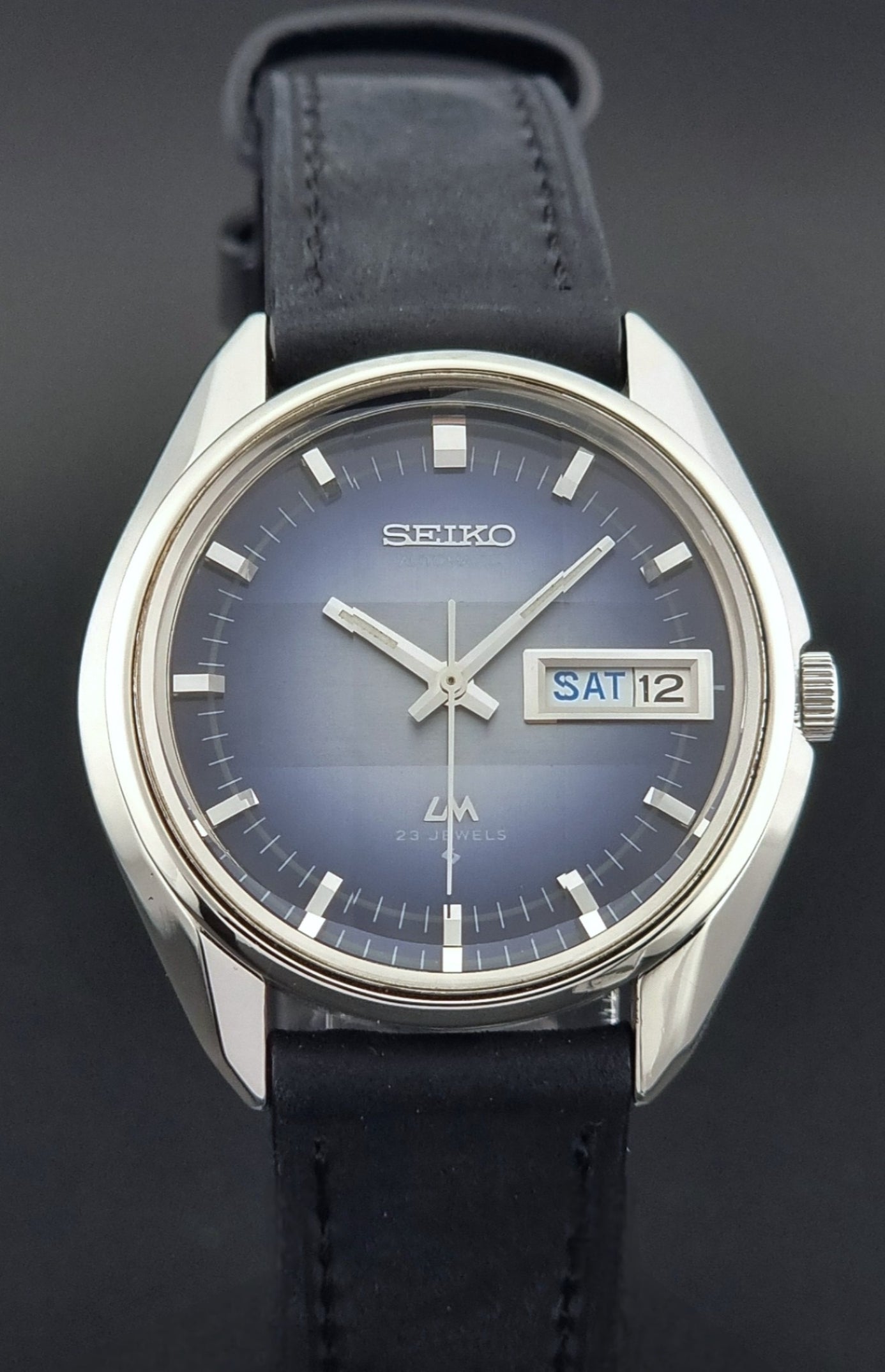 Seiko watch with blue face and black leather strap on a dark background