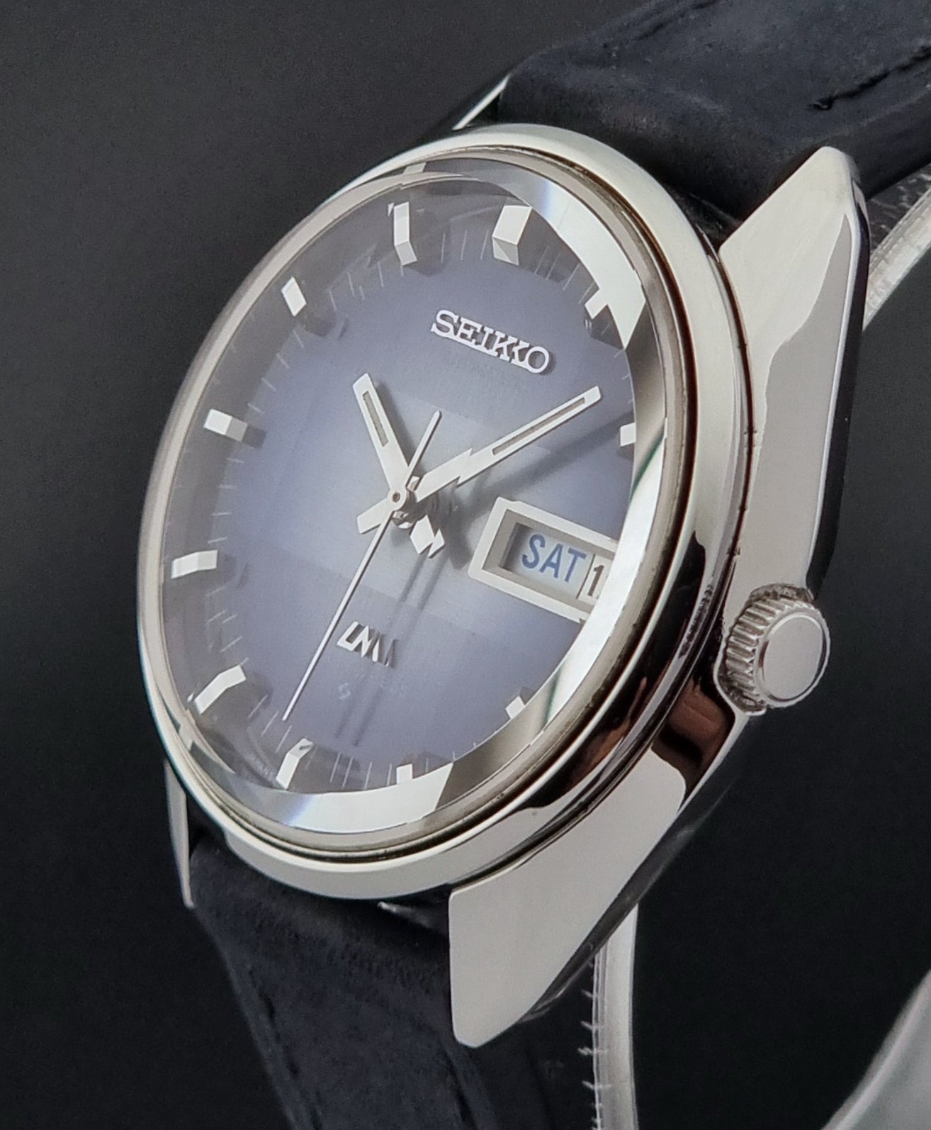 Seiko watch with blue face and black strap on a dark background