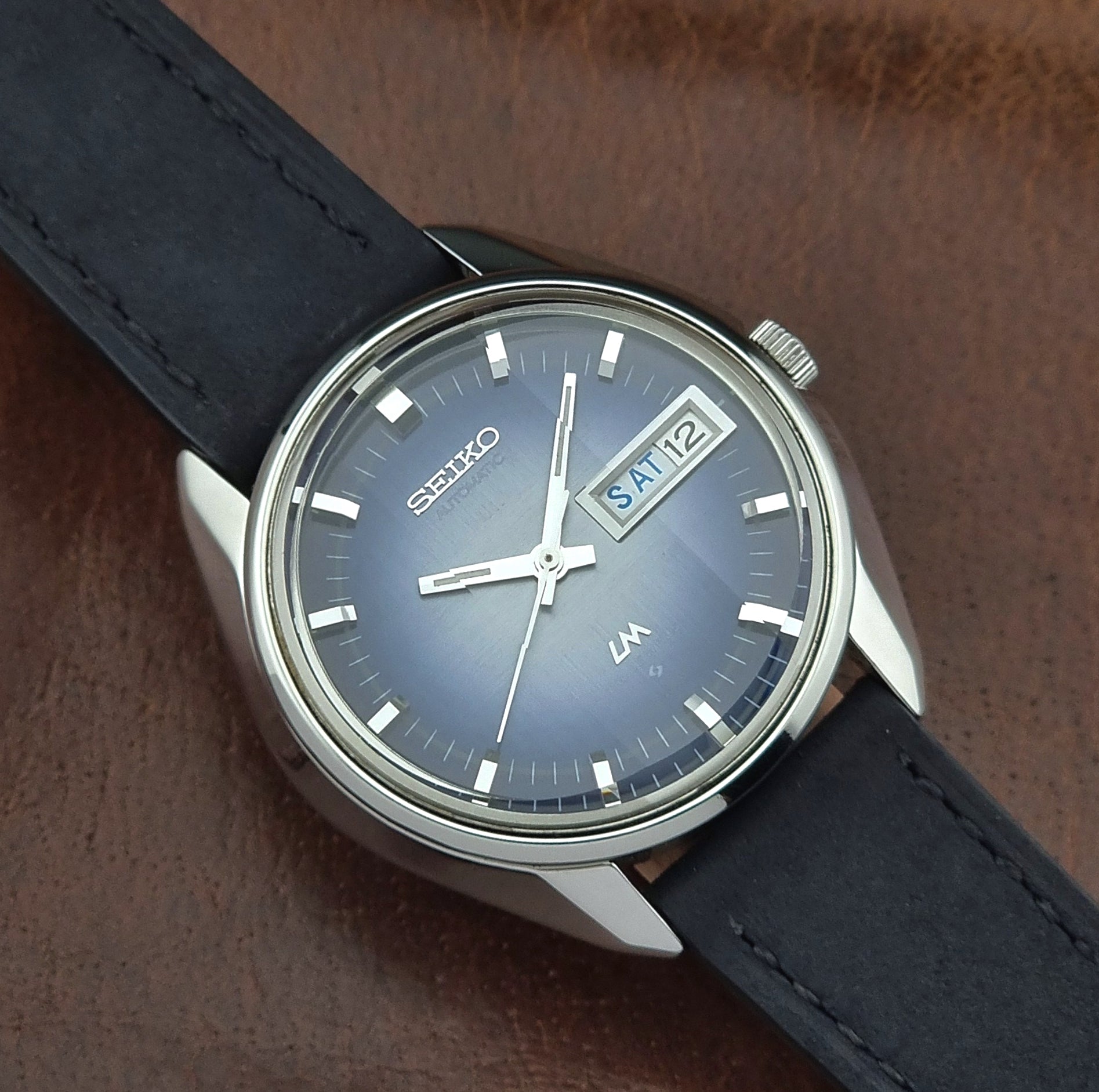 Seiko watch with blue face and dark leather strap on brown background