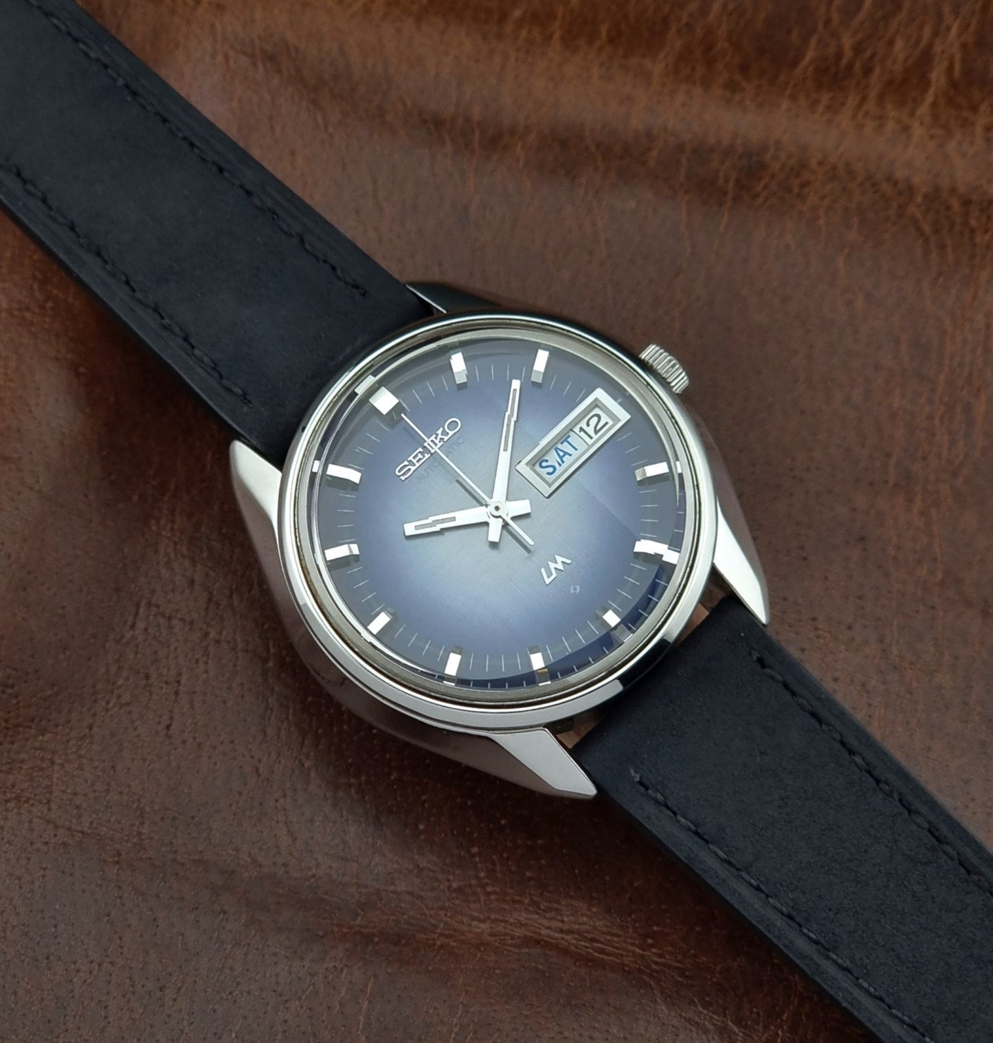Seiko watch with blue face and black leather strap on brown leather background