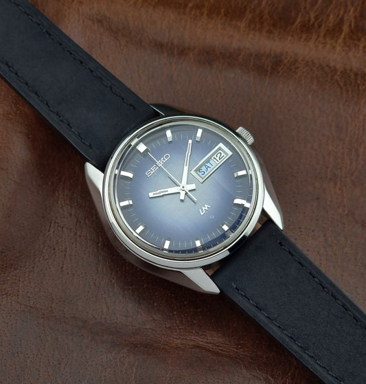 Seiko watch with blue face and black leather strap on brown leather background