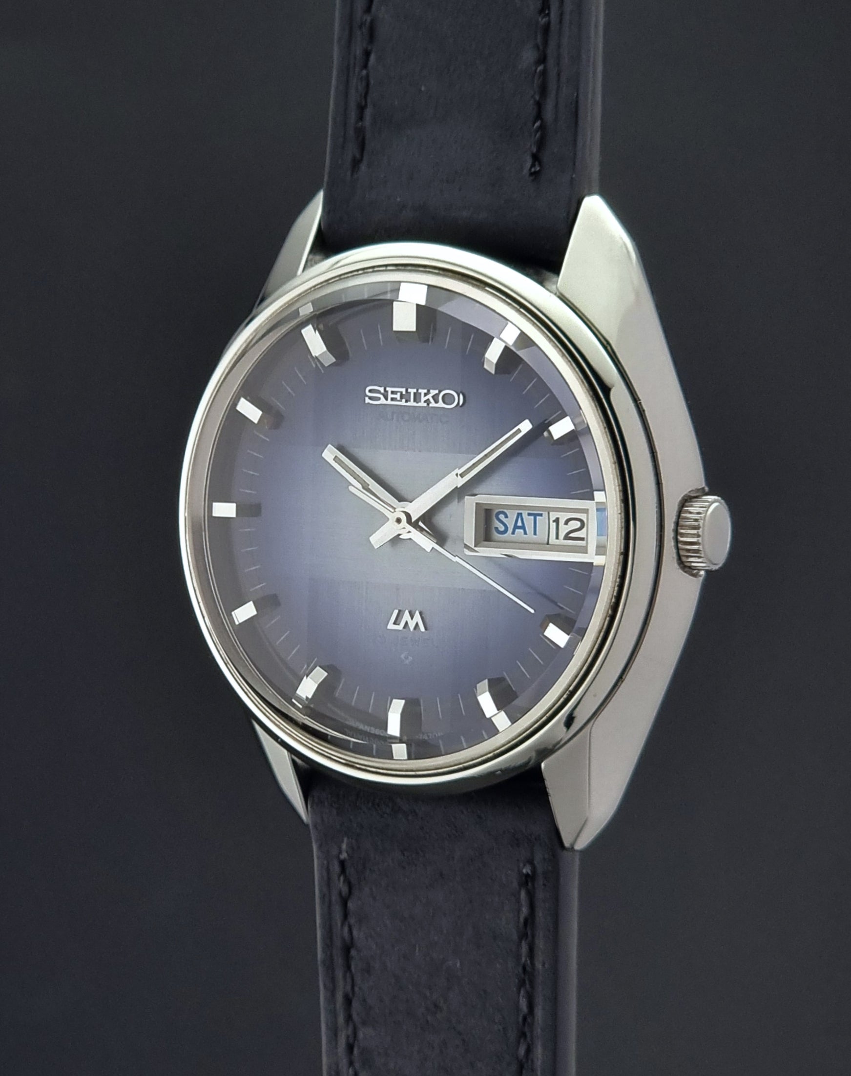 Seiko watch with blue face and black leather strap on a dark background