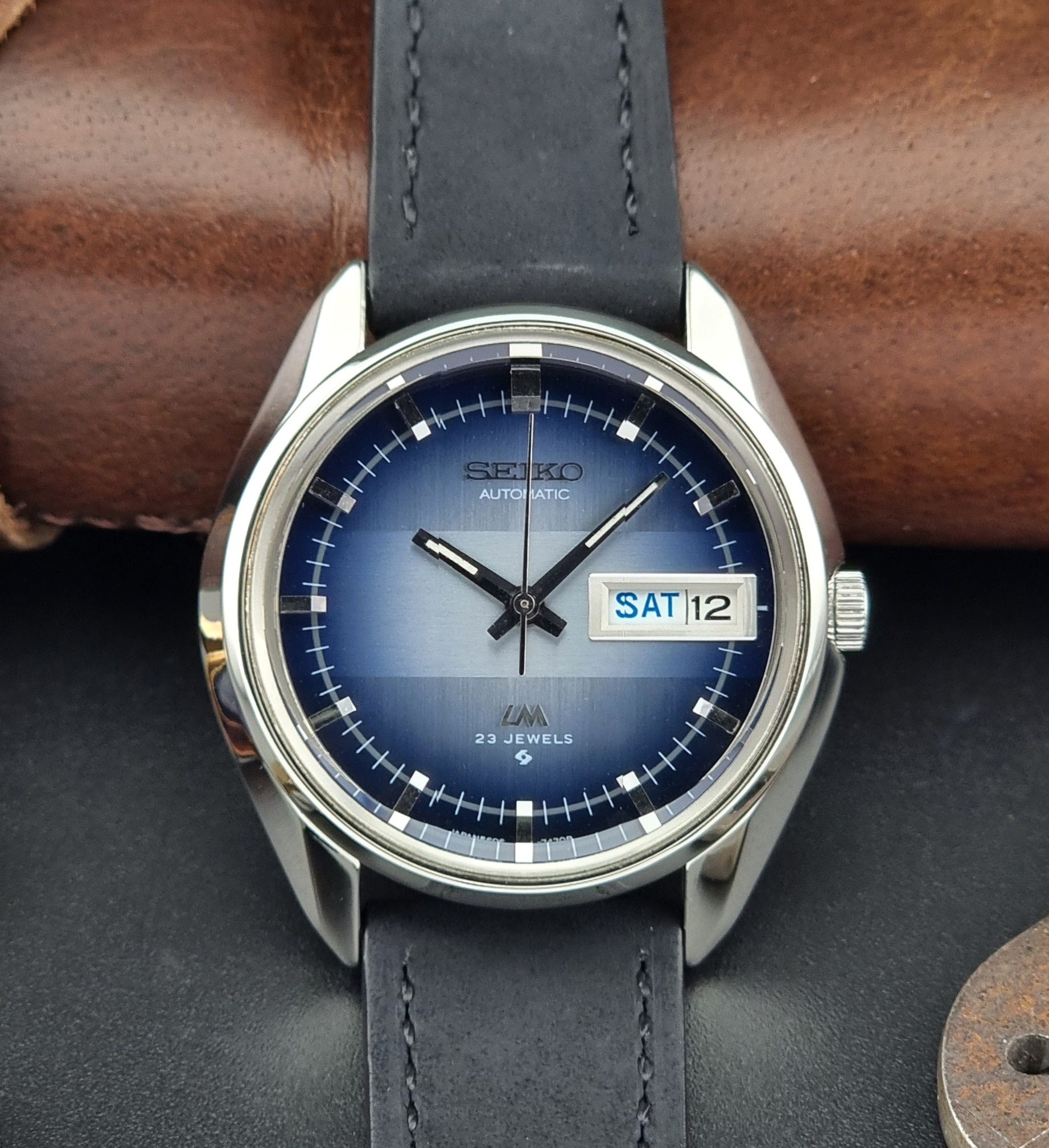 Seiko watch with blue dial and leather strap on a dark surface
