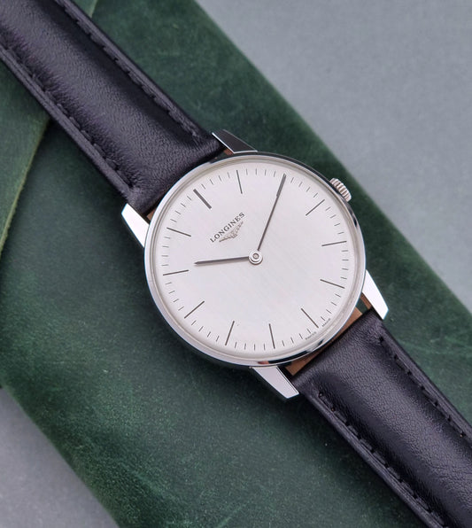 Vintage Longines watch with black leather strap on a green surface