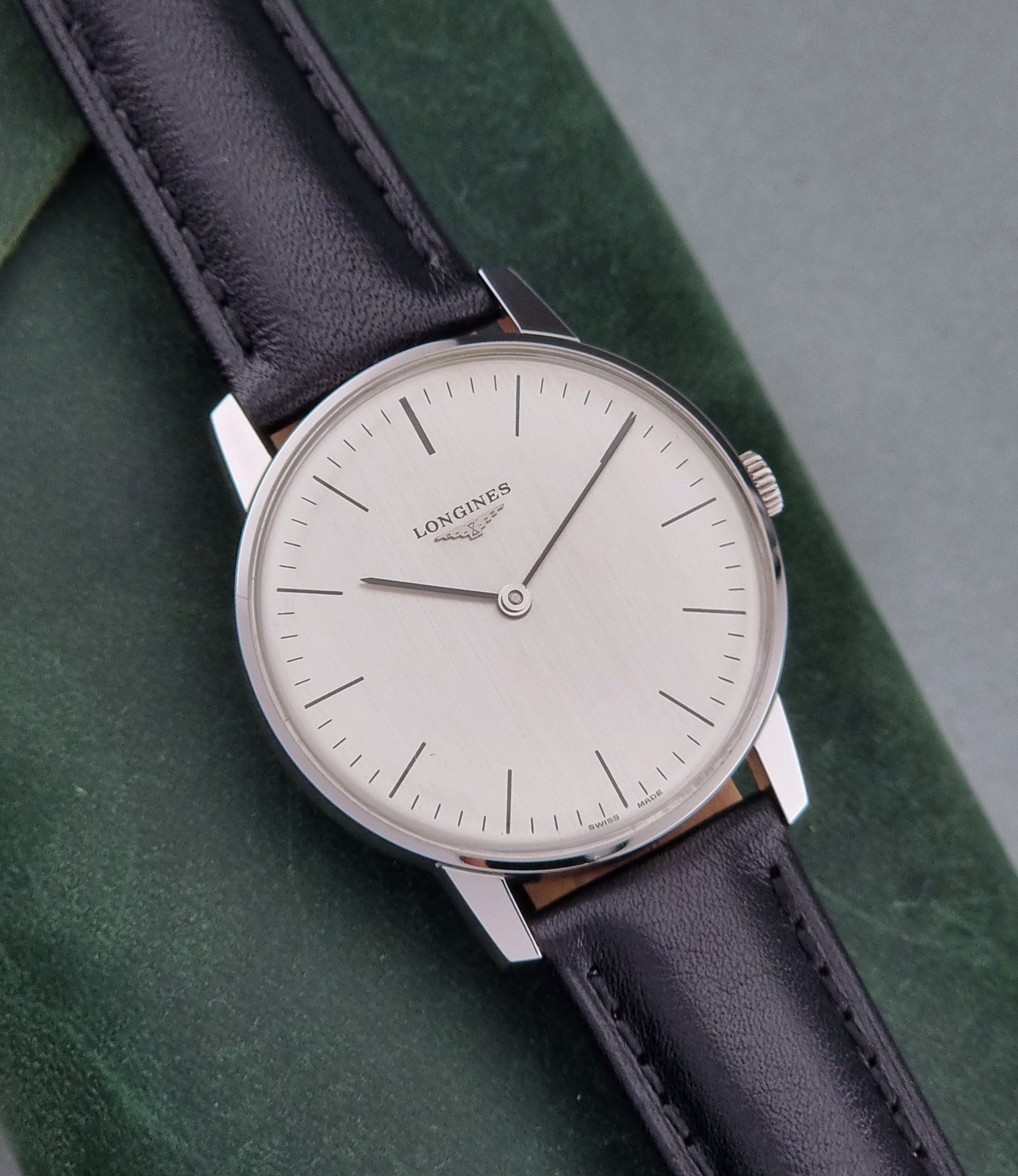 Vintage Longines watch with black leather strap on a green surface