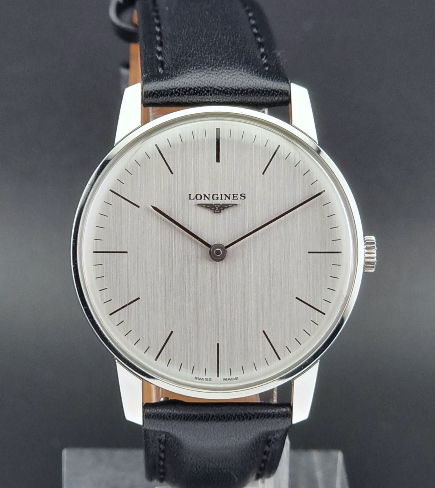 Vintage Longines watch with black leather strap on a green surface