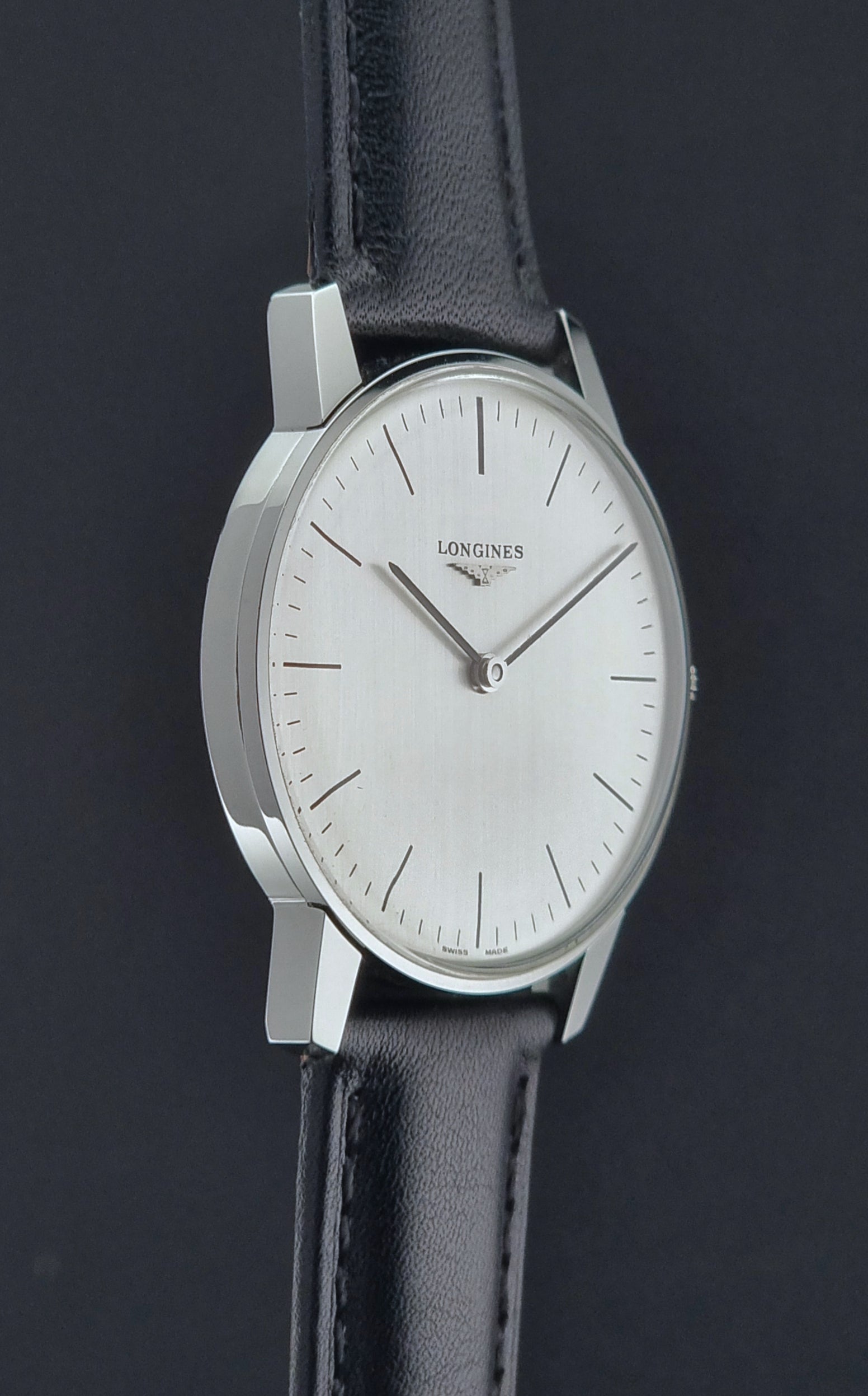 Vintage Longines watch with black leather strap on a grey surface