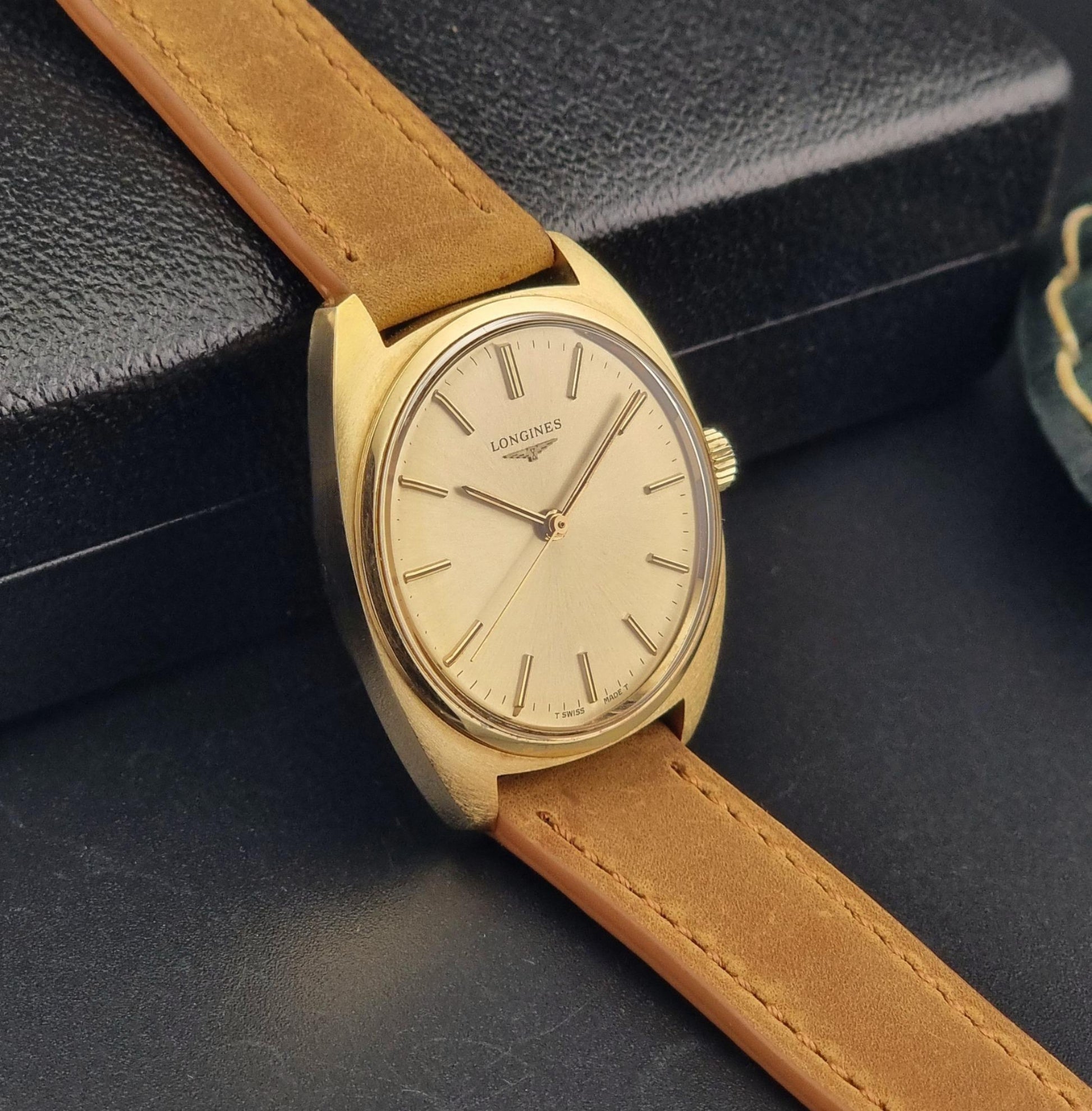 Vintage Gold Longines wristwatch with brown leather strap on a dark surface