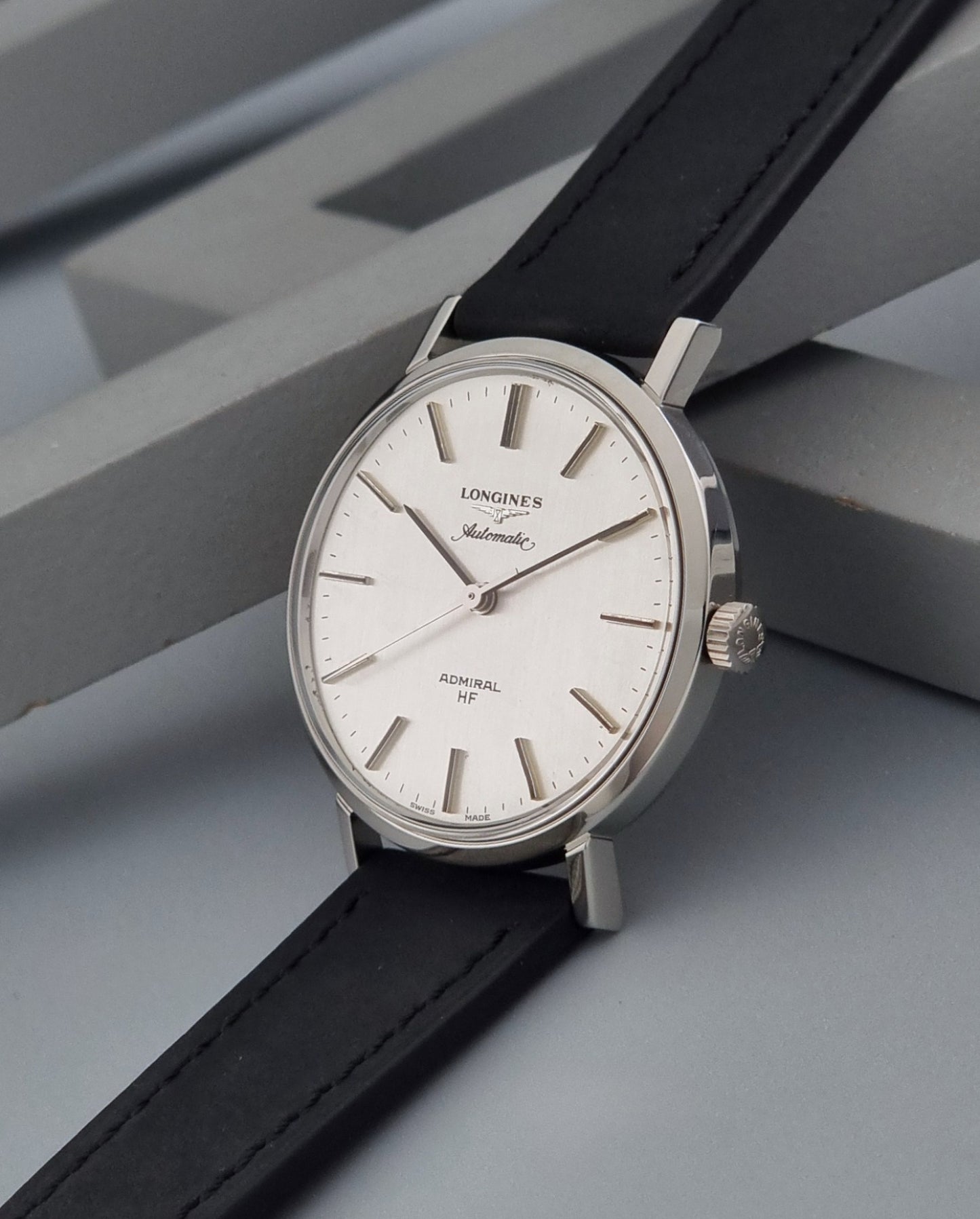 Vintage Longines Admiral Hi frequency Automatic Wristwatch 2305-1 with a black leather strap on a grey background crown view