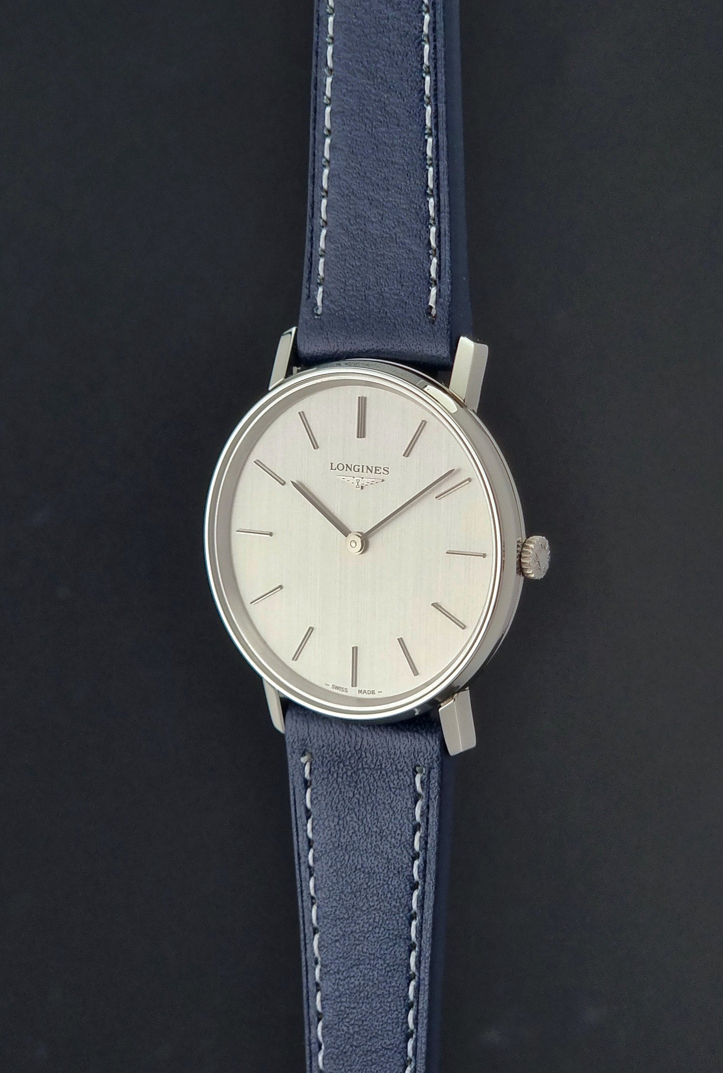 Vintage Longines Wristwatch 4127  with blue strap and silver case on a dark gray background crown profile view