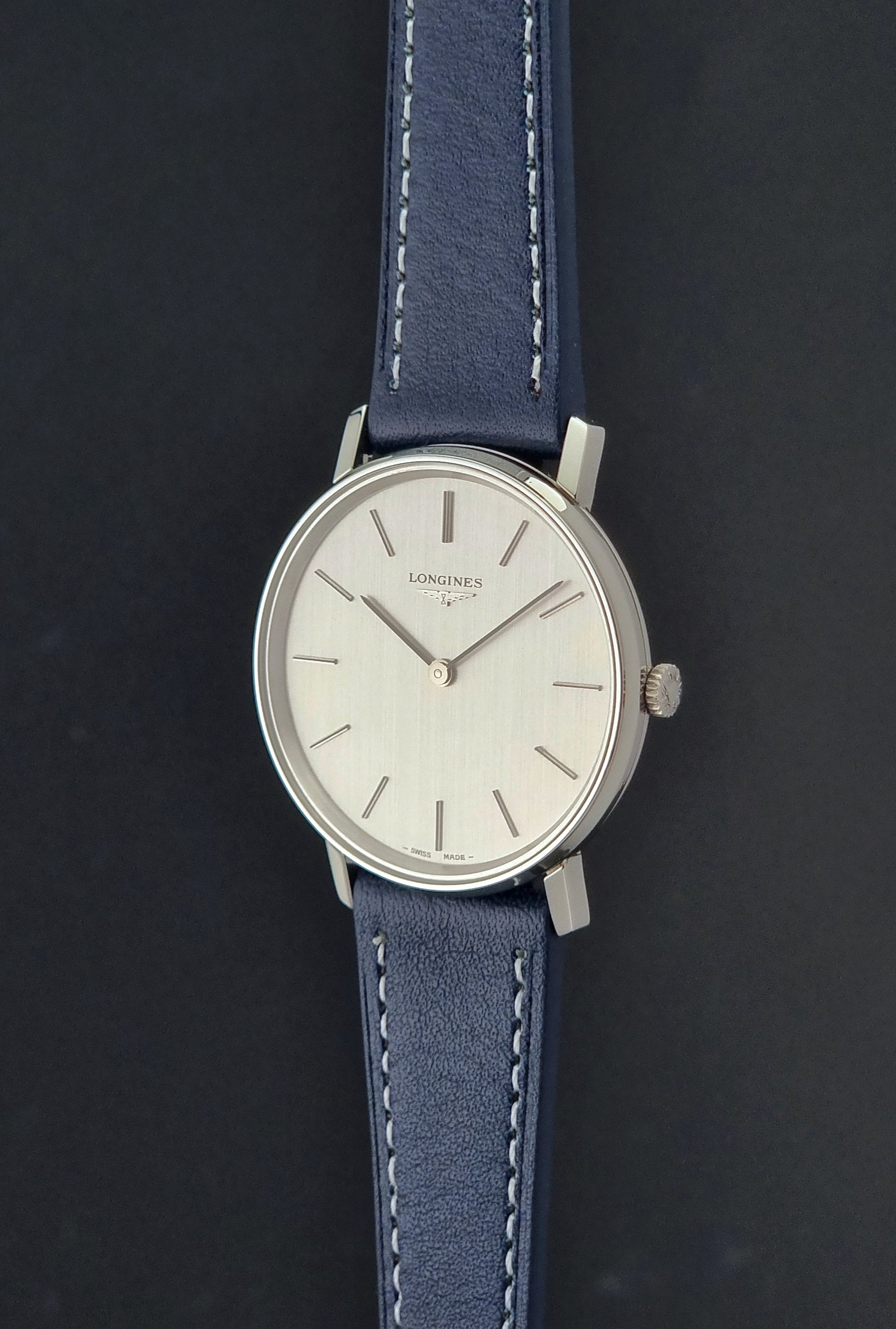 Vintage Longines Wristwatch 4127  with blue strap and silver case on a dark gray background crown profile view