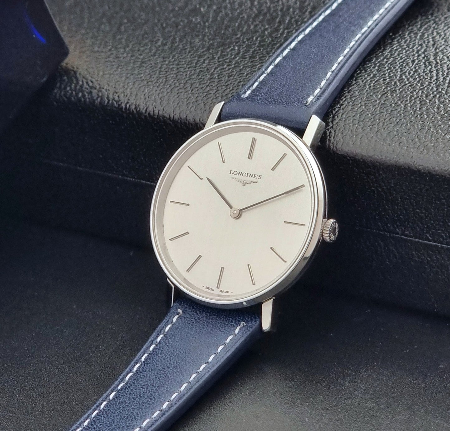 Vintage Longines Wristwatch 4127  with blue strap and silver case on a dark gray background crown view