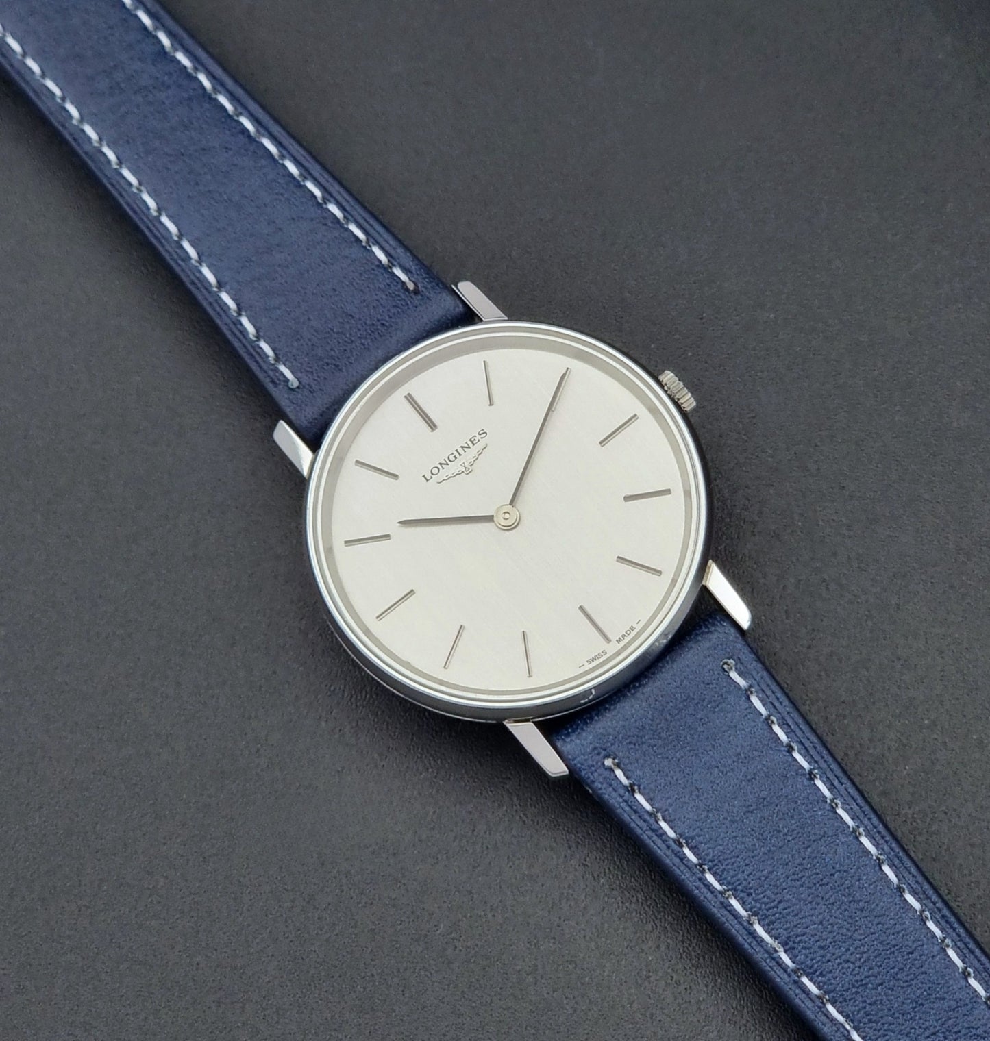 Vintage Longines Wristwatch 4127  with blue strap and silver case on a dark gray background close up dial view