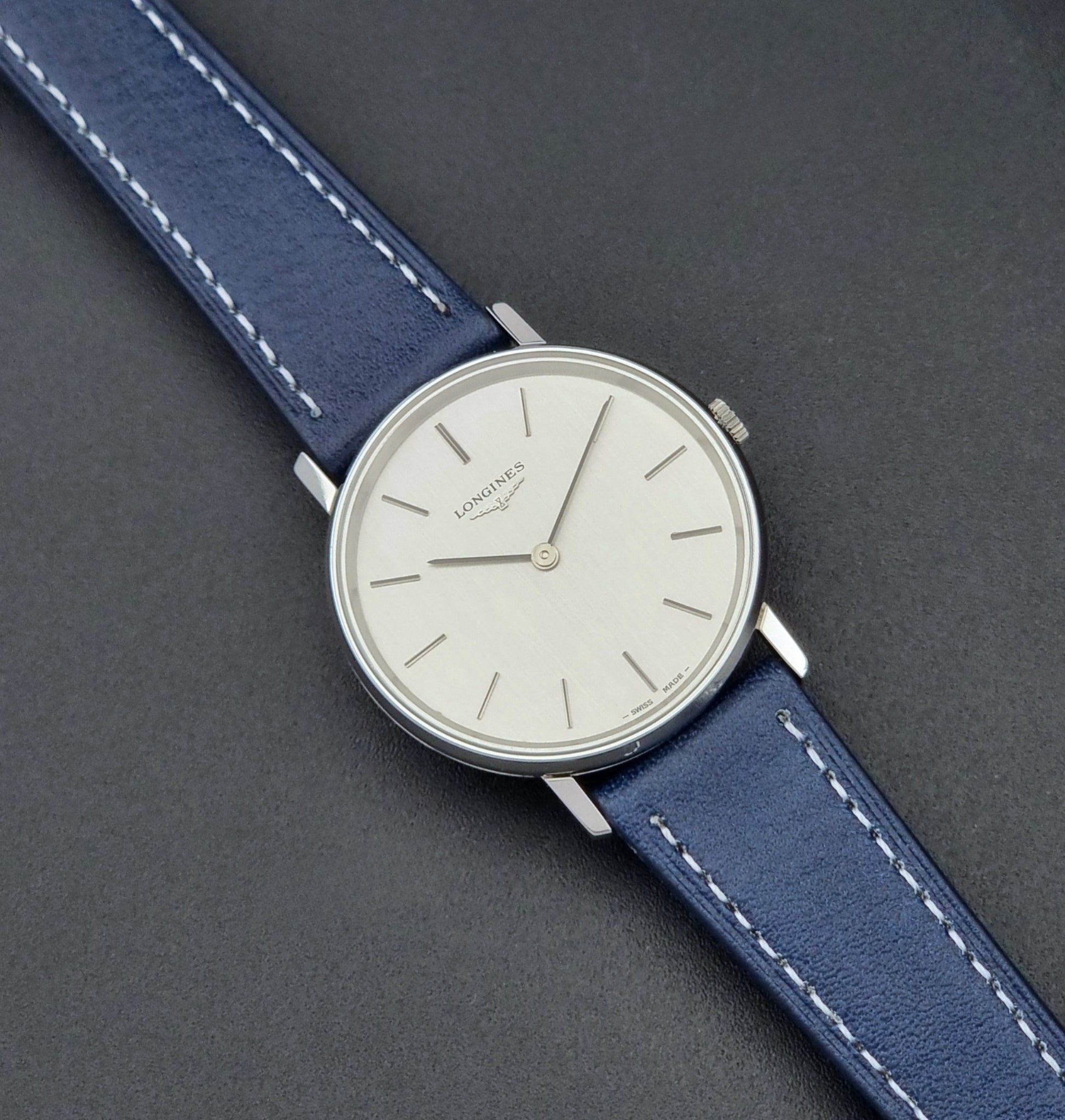 Vintage Longines Wristwatch 4127  with blue strap and silver case on a dark gray background close up dial view
