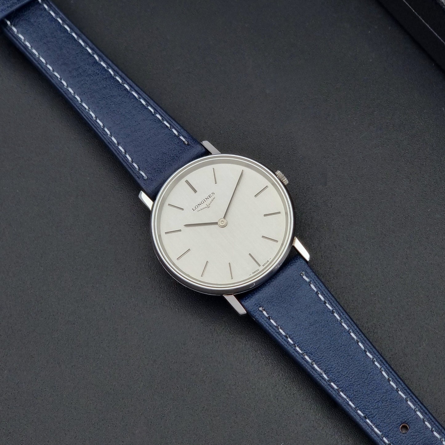 Vintage Longines Wristwatch 4127  with blue strap and silver case on a dark gray background dial