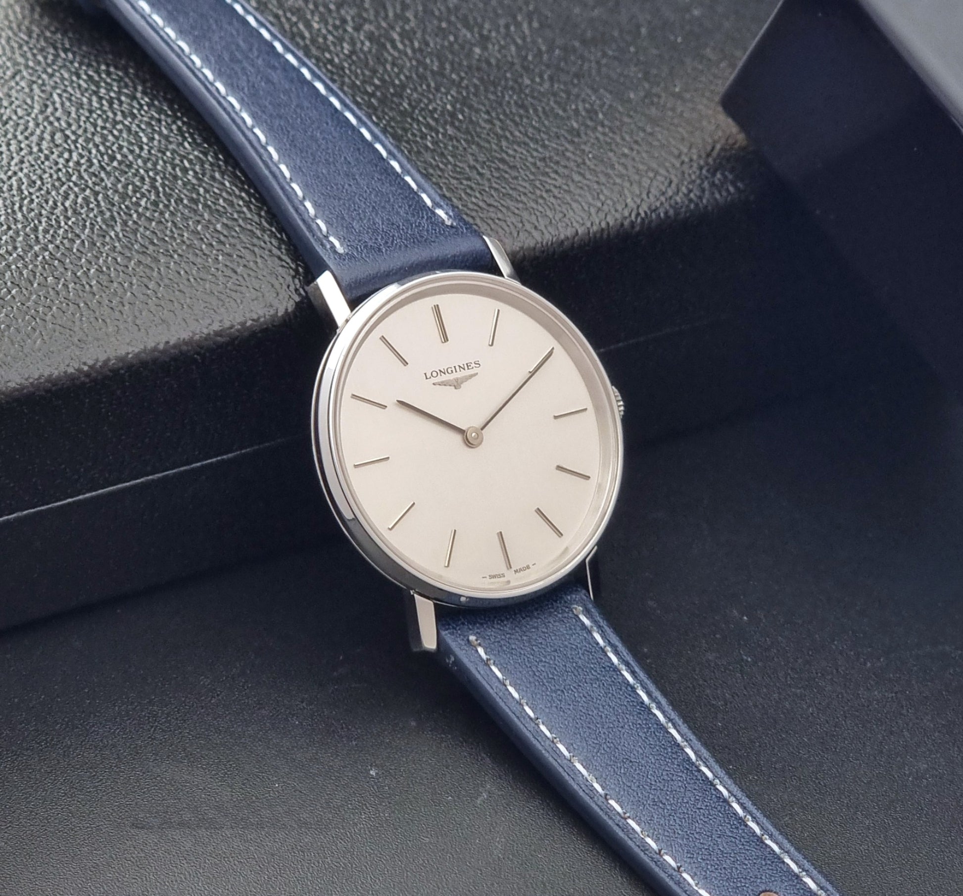 Vintage Longines Wristwatch 4127  with blue strap and silver case on a dark gray background side view