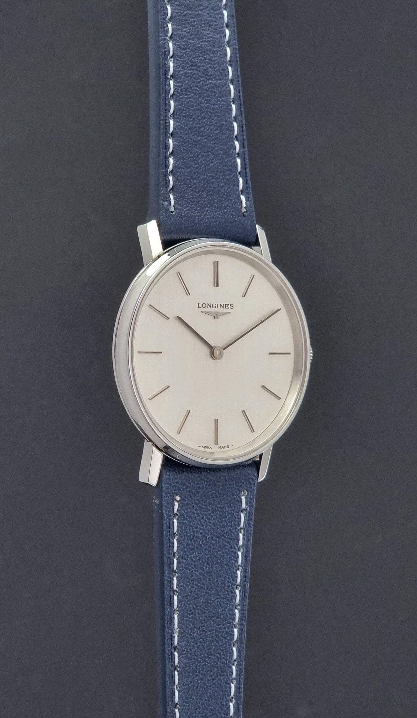 Vintage Longines Wristwatch 4127  with blue strap and silver case on a dark gray background side profile view