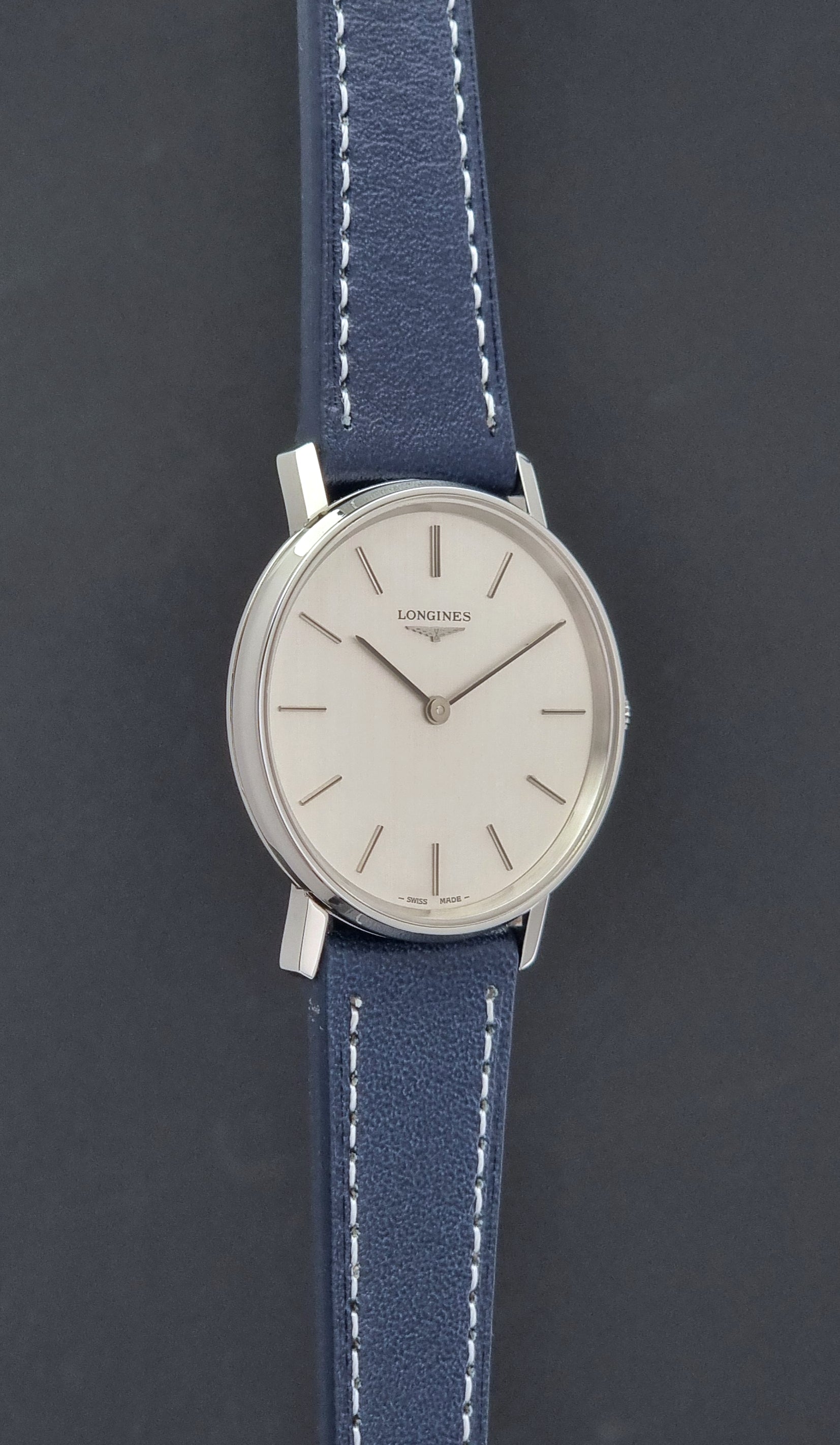 Vintage Longines Wristwatch 4127  with blue strap and silver case on a dark gray background side profile view