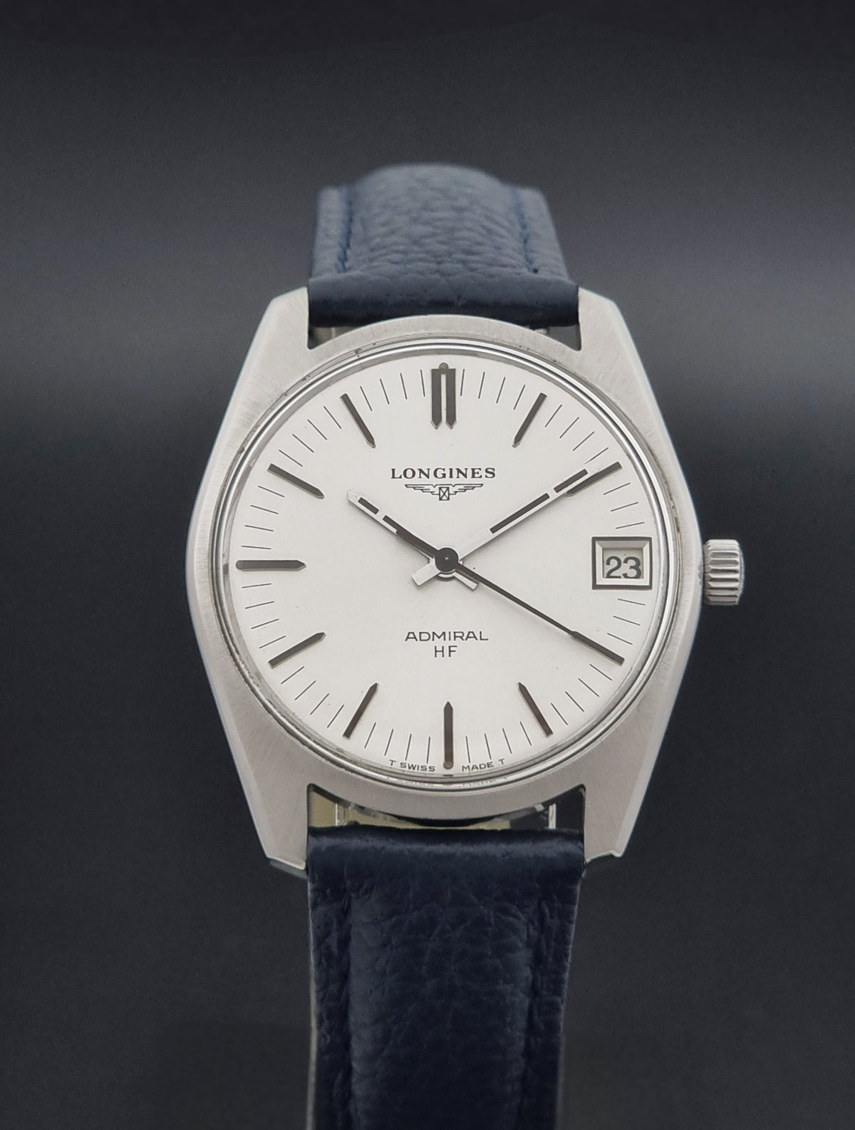 A vintage Longines Admiral HF wristwatch with a silver-toned metal case, white dial, and dark blue leather strap, shown against a dark gray background.