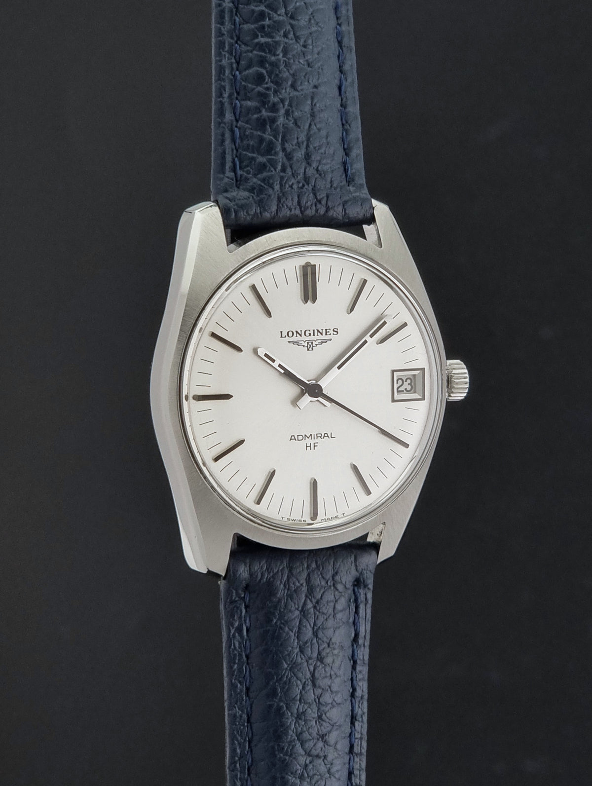 A Longines Admiral HF wristwatch with a silver-toned stainless steel case, white dial, and textured navy blue leather strap, shown against a dark gray background.