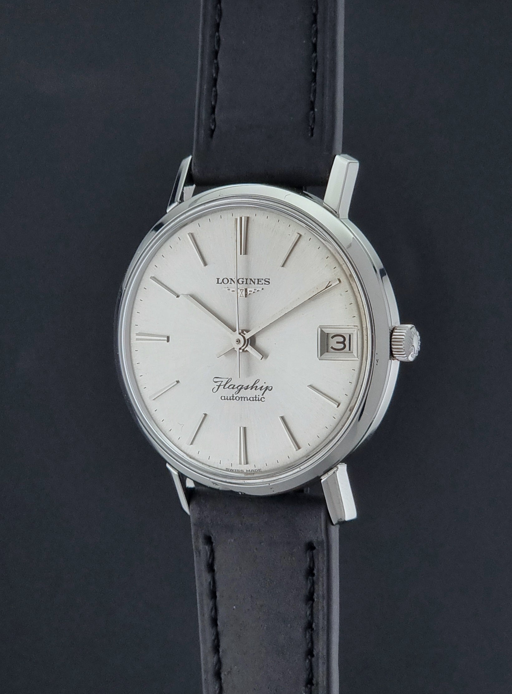 Vintage Longines Flagship watch with a silver dial and black leather strap on a dark background