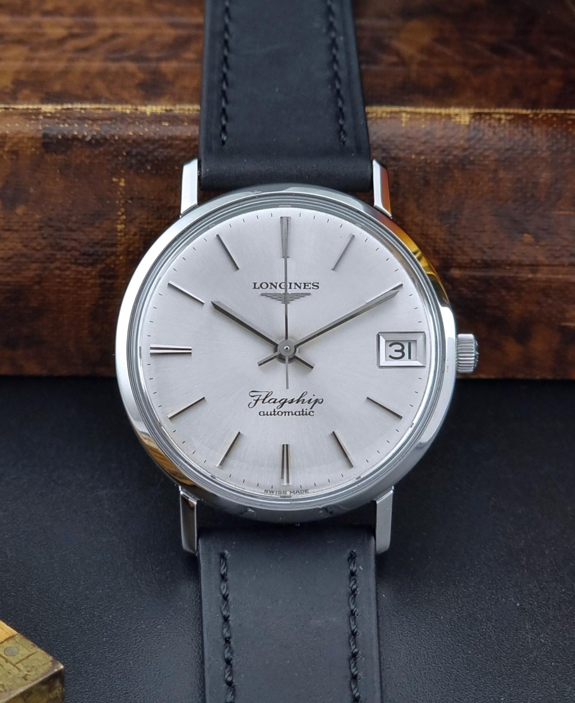 Front view of a Vintage Longines Flagship watch with silver dial and black leather strap on a dark surface