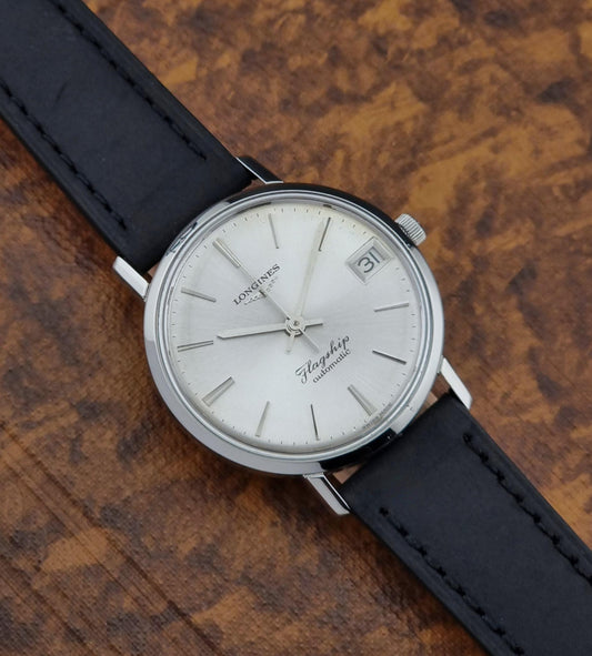 Vintage Longines Flagship Wristwatch with black strap and silver case on a wooden surface