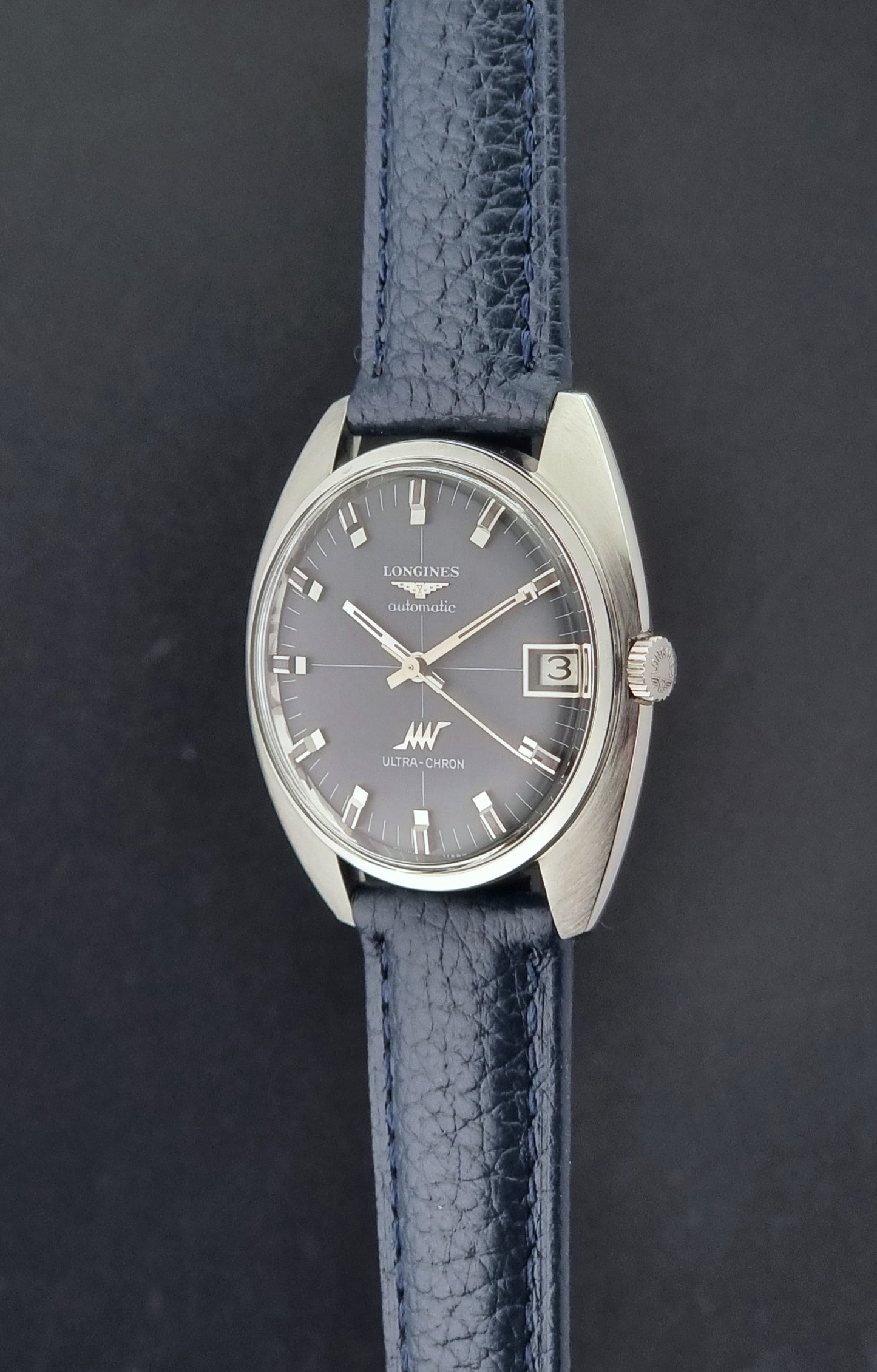 Vintage Longines watch ULTRA-CHRON 8071-2 with blue leather strap and silver case on a dark gray background crown profile view