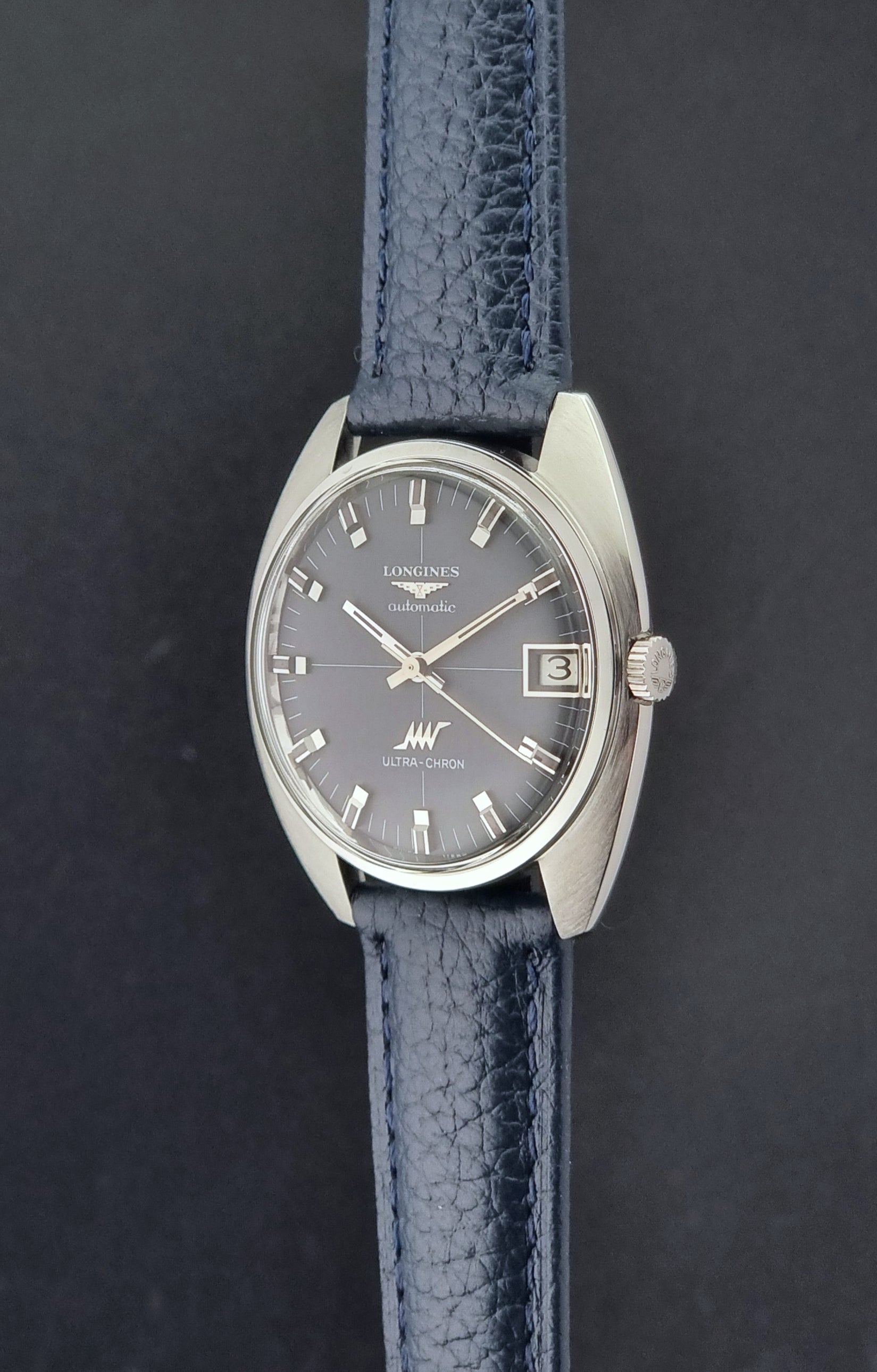 Vintage Longines watch ULTRA-CHRON 8071-2 with blue leather strap and silver case on a dark gray background crown profile view