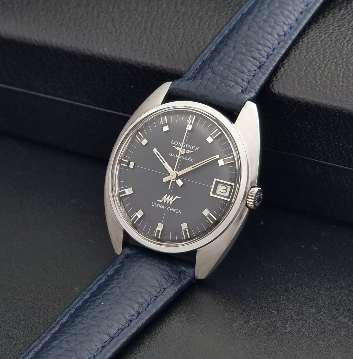 Vintage Longines watch ULTRA-CHRON 8071-2 with blue leather strap and silver case on a dark gray background crown view