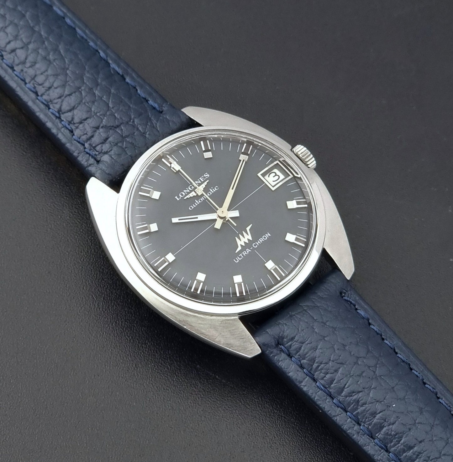 Vintage Longines watch ULTRA-CHRON 8071-2 with blue leather strap and silver case on a dark gray background close up dial view
