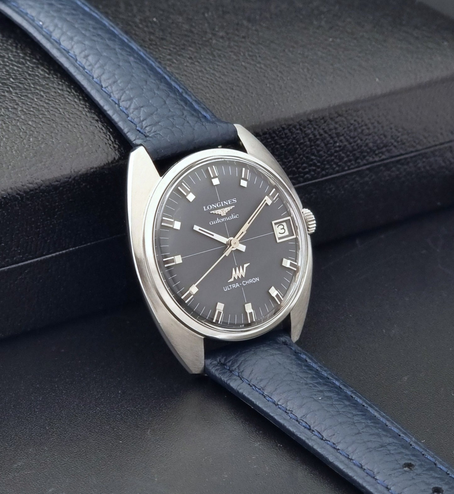 Vintage Longines watch ULTRA-CHRON 8071-2 with blue leather strap and silver case on a dark gray background side view