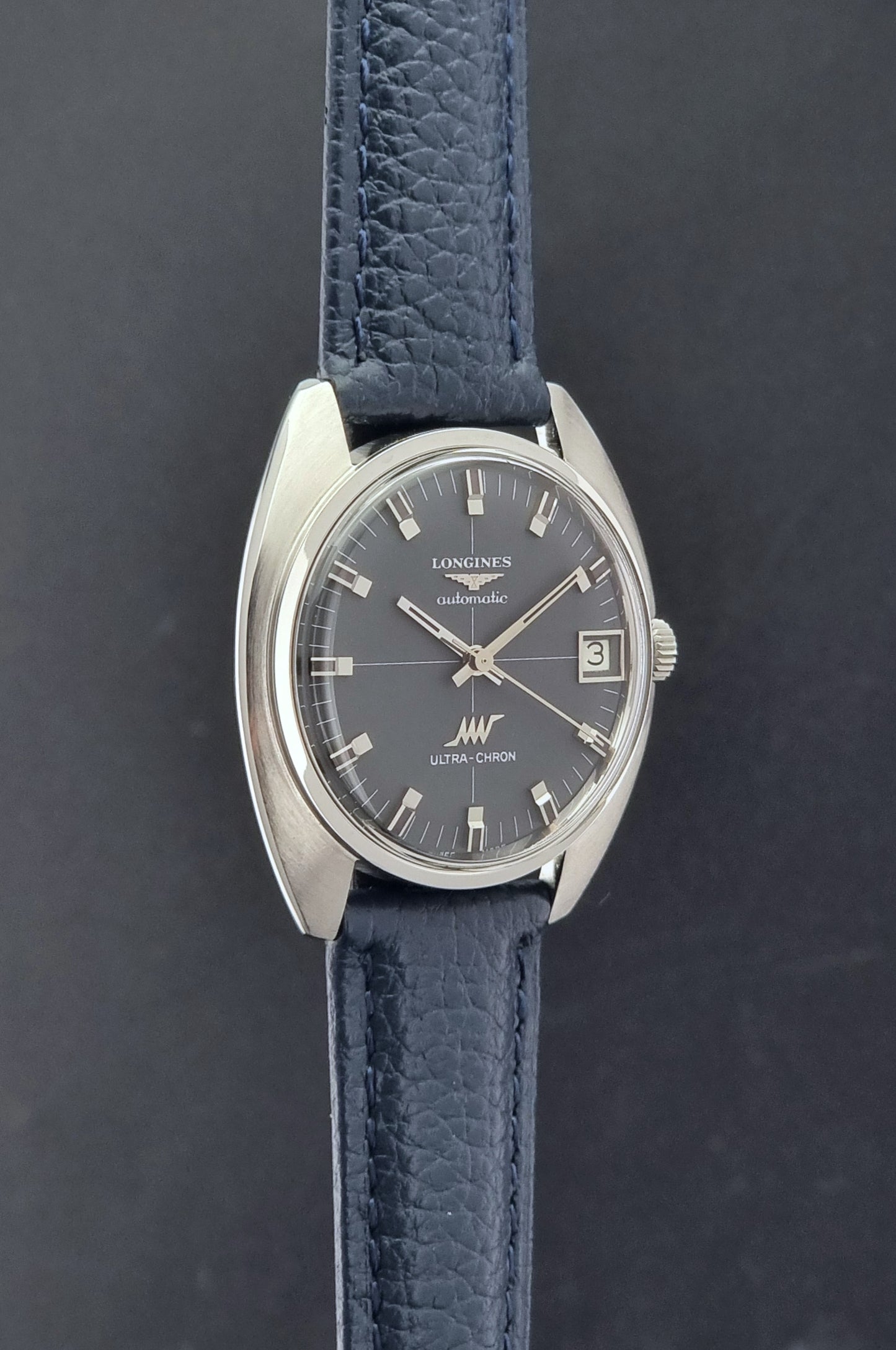 Vintage Longines watch ULTRA-CHRON 8071-2 with blue leather strap and silver case on a dark gray background side profile view