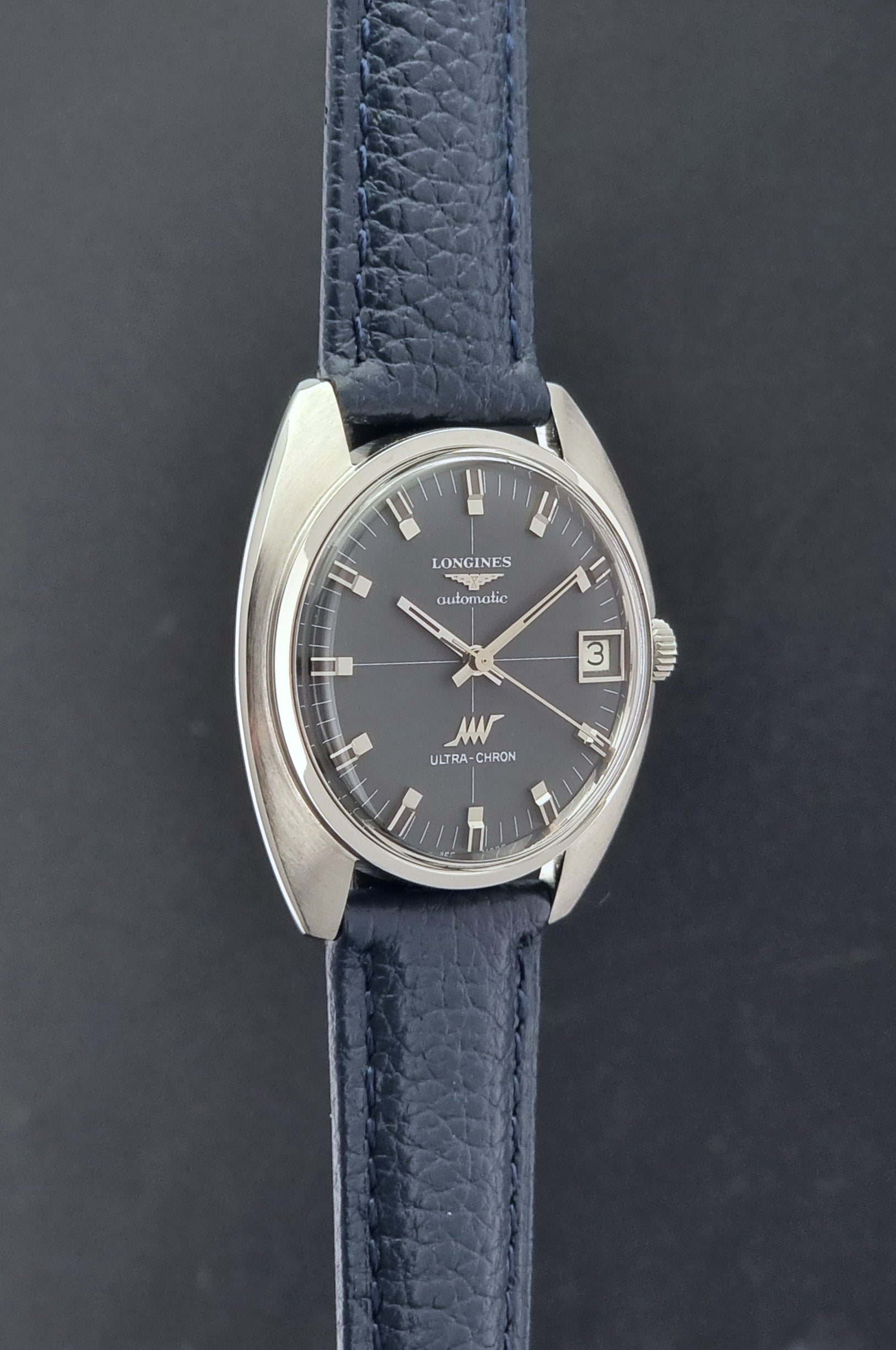 Vintage Longines watch ULTRA-CHRON 8071-2 with blue leather strap and silver case on a dark gray background side profile view