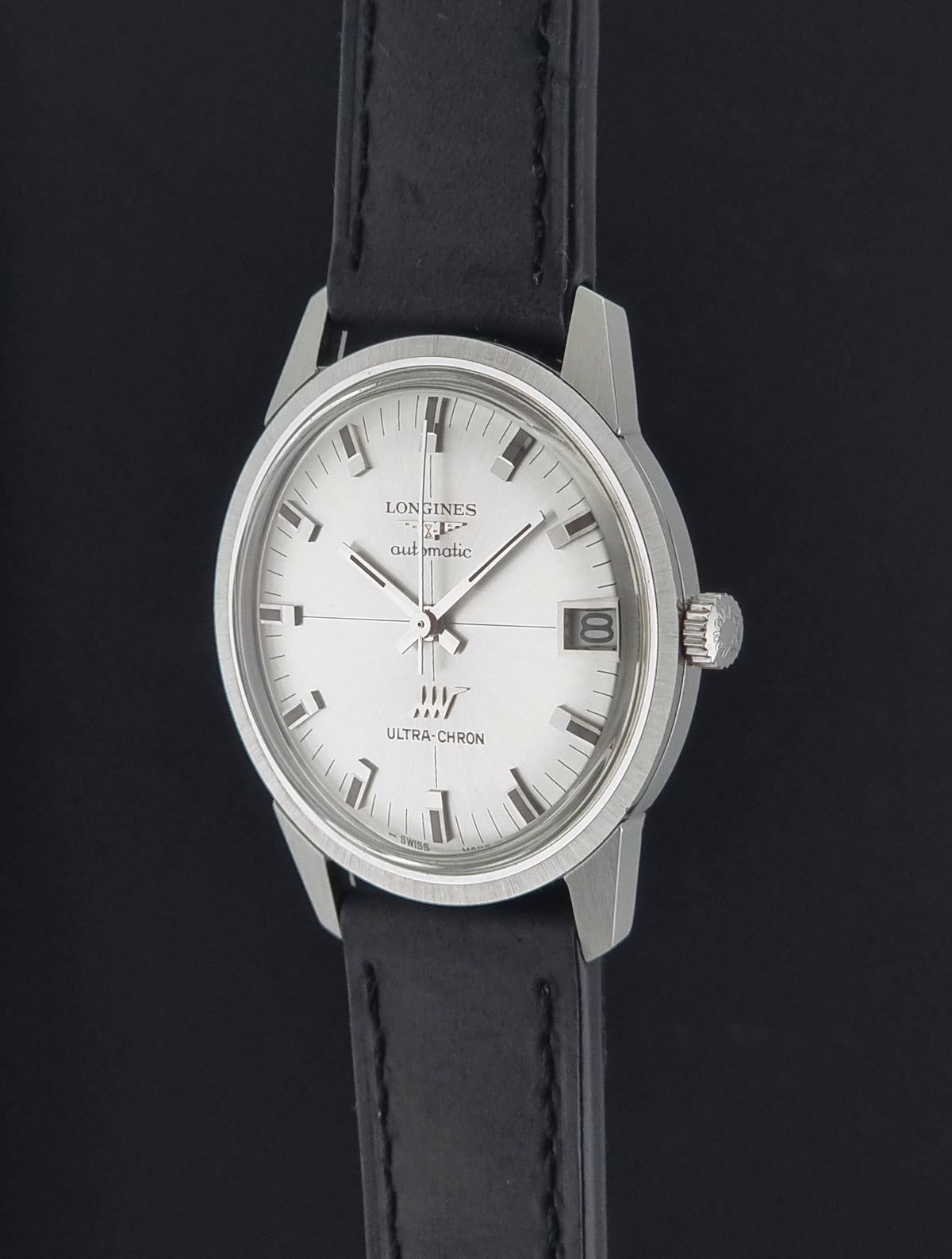 A vintage Longines wristwatch with a silver-toned stainless steel case, white dial, and black leather strap, shown against a dark background.