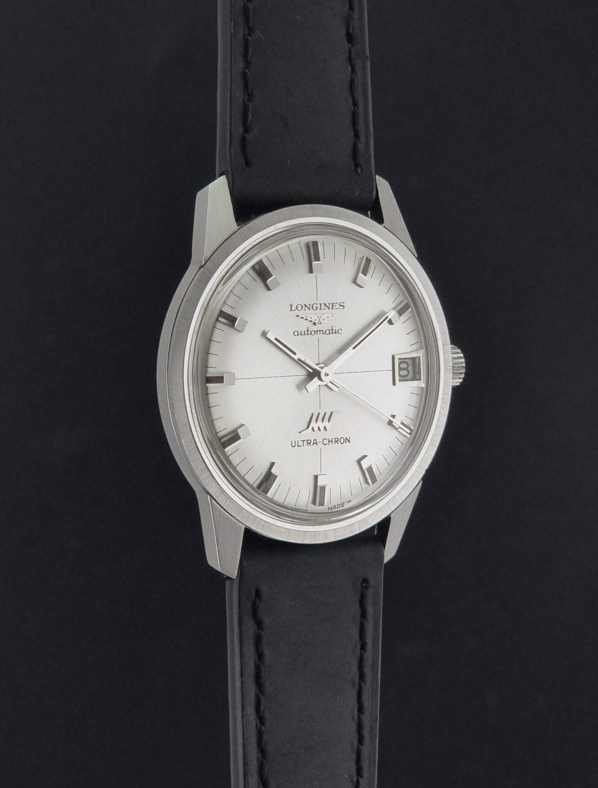 Vintage Longines ULTRA-CHRON 8309 watch with a silver-toned metal case, white dial, and black leather strap, shown against a dark background.