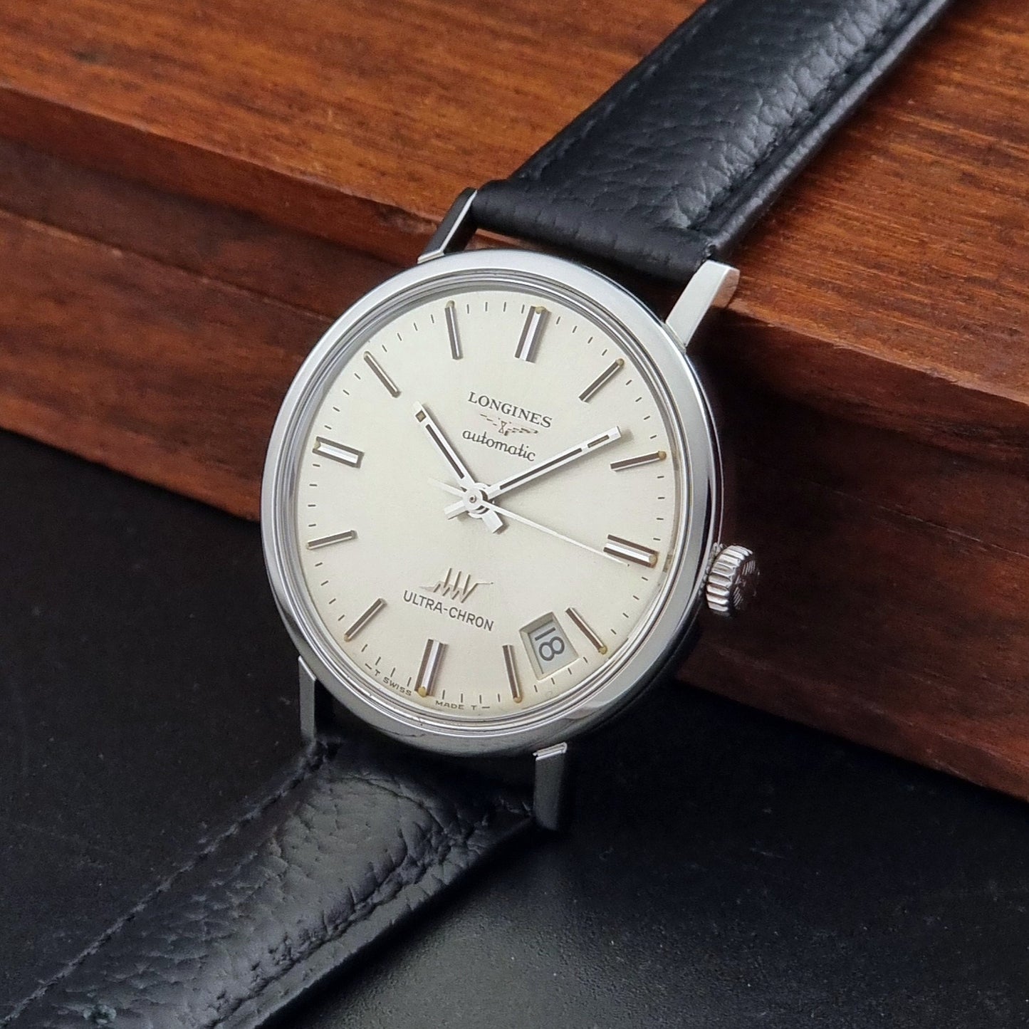 Vintage Longines ULTRA-CHRON 8383-1 with black leather strap and silver case on a dark gray background crown view