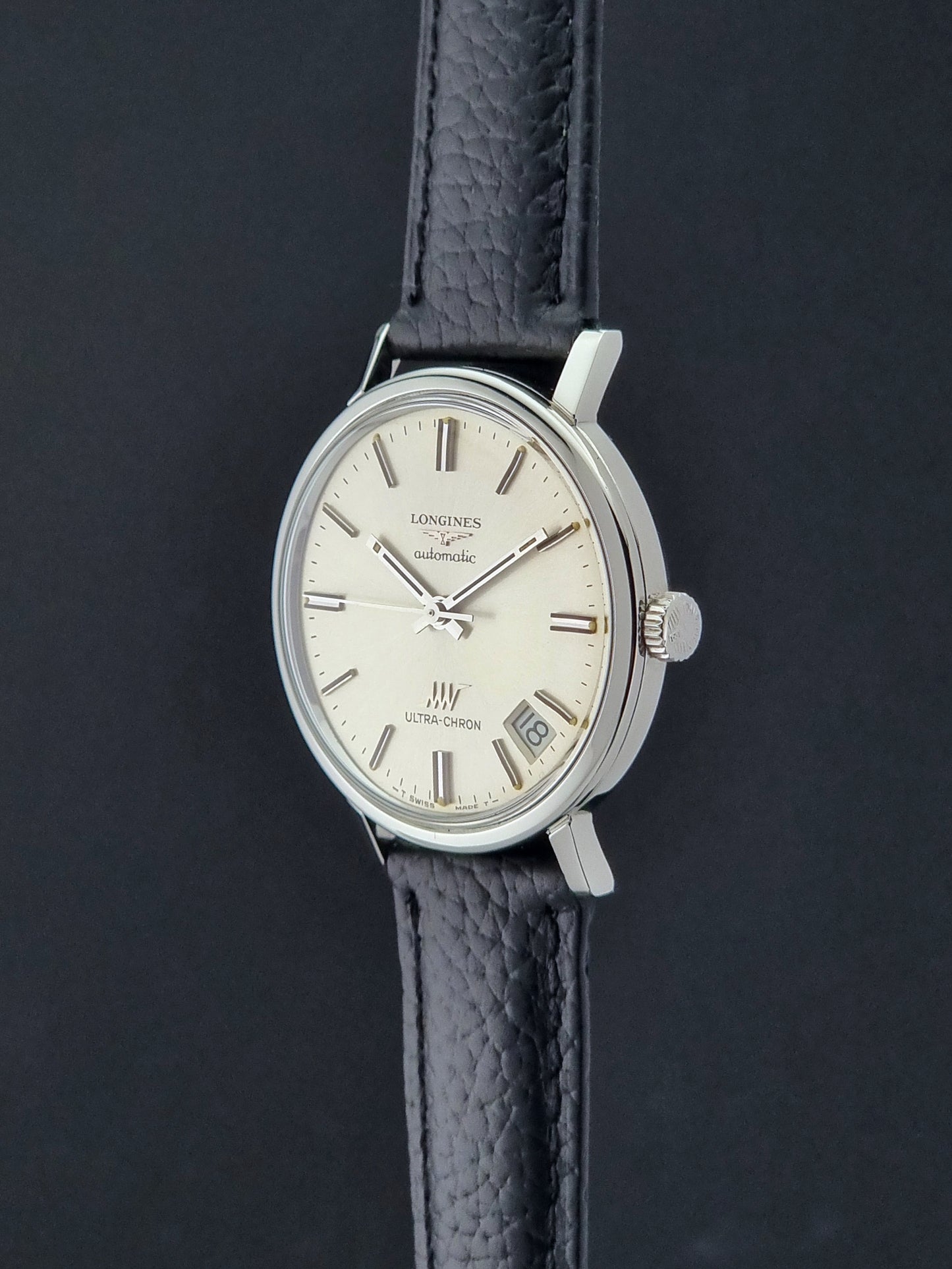 Vintage Longines ULTRA-CHRON 8383-1 with black leather strap and silver case on a dark gray background crown profile view