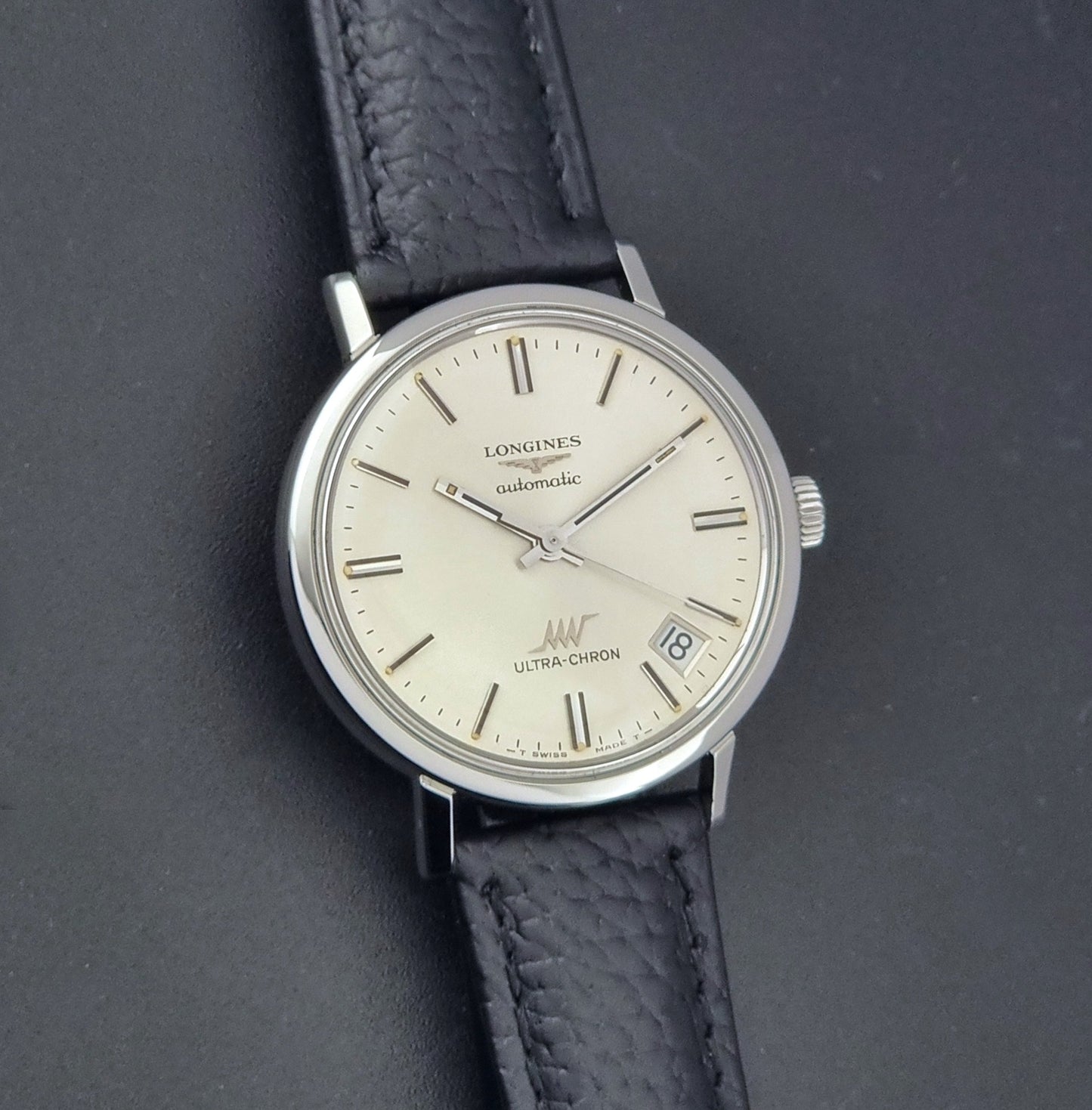 Vintage Longines ULTRA-CHRON 8383-1 with black leather strap and silver case on a dark gray background front view