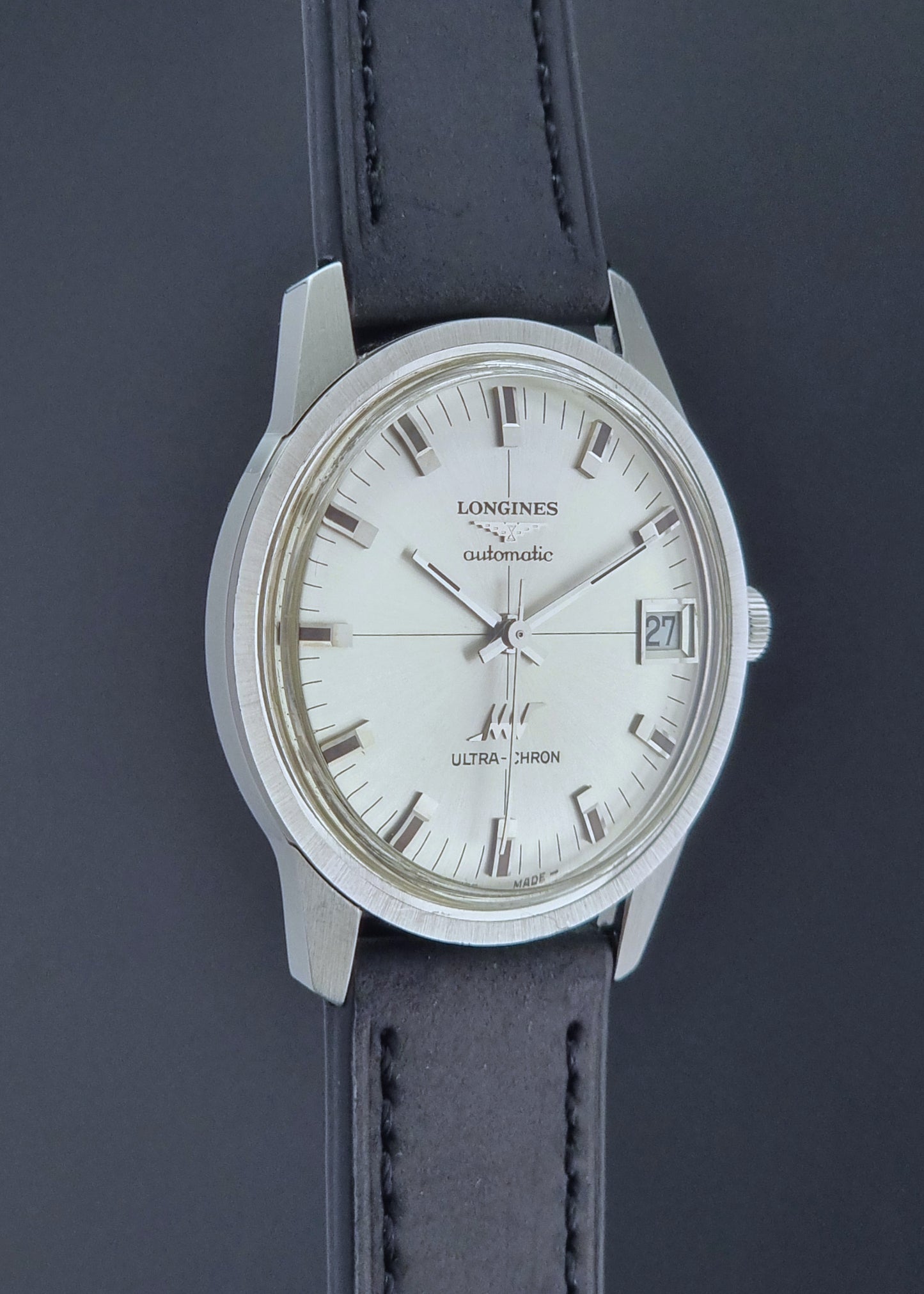 Longines watch with a silver dial and black leather strap on a dark background
