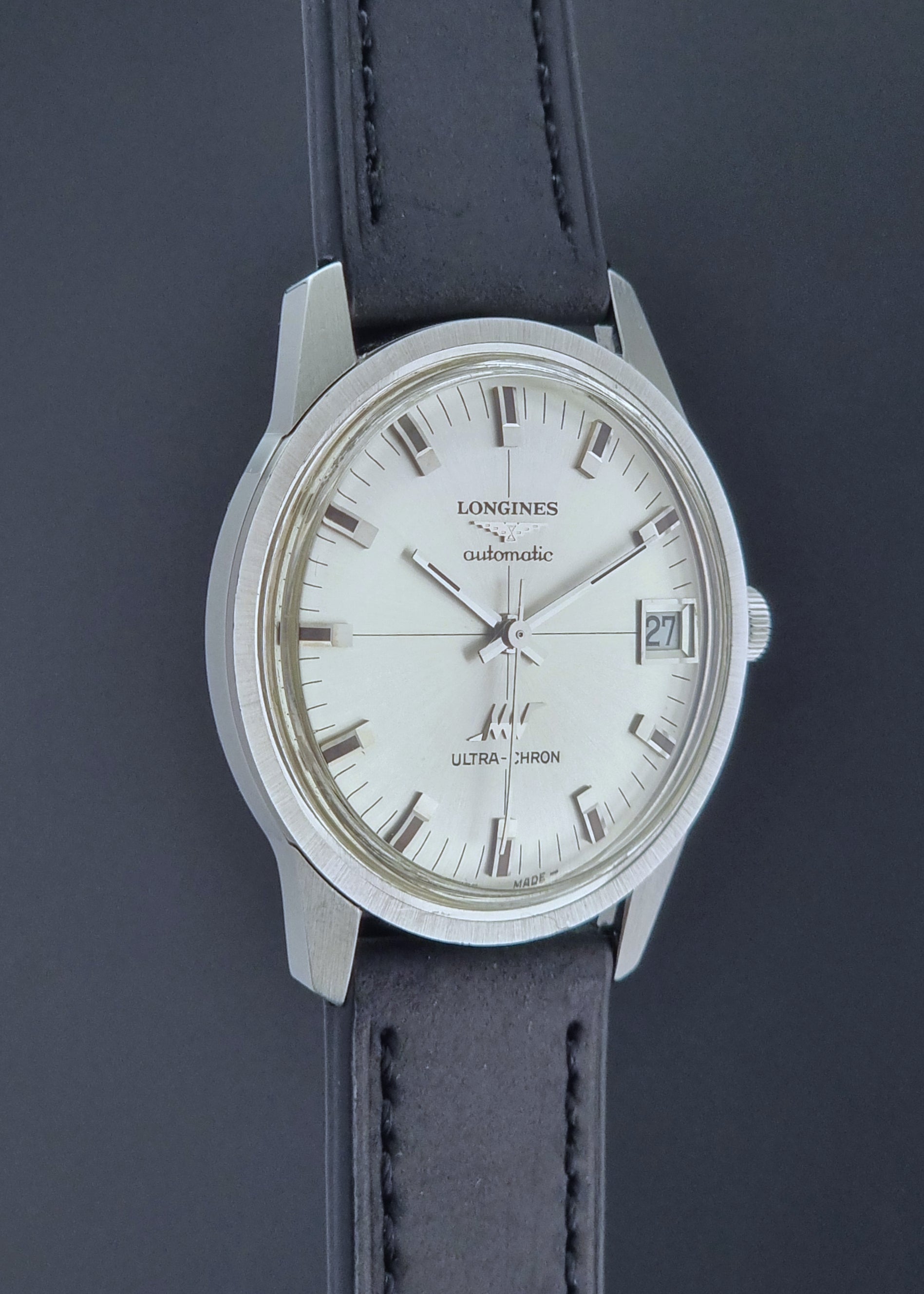 Longines watch with a silver dial and black leather strap on a dark background