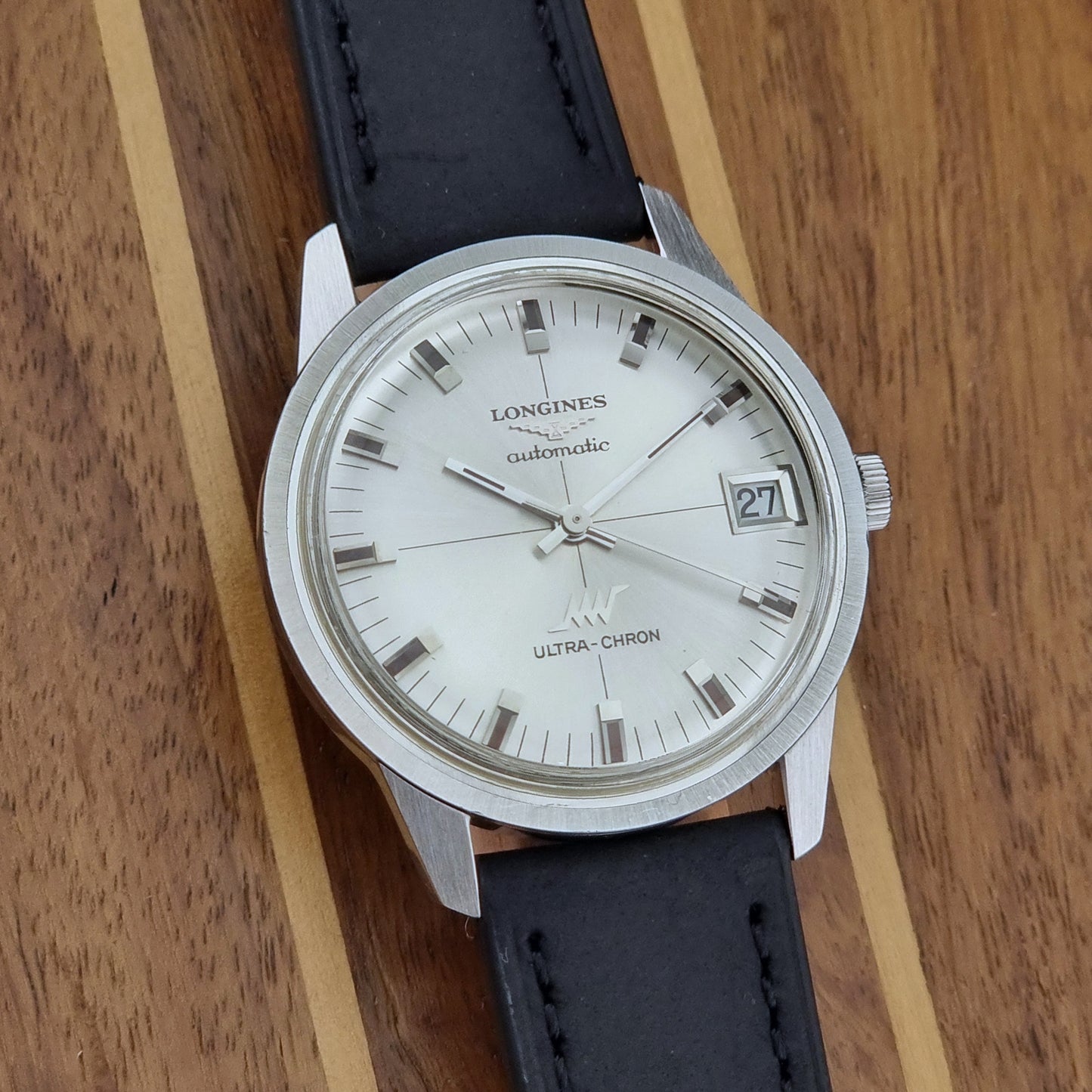 Longines watch with black leather strap on a wooden surface